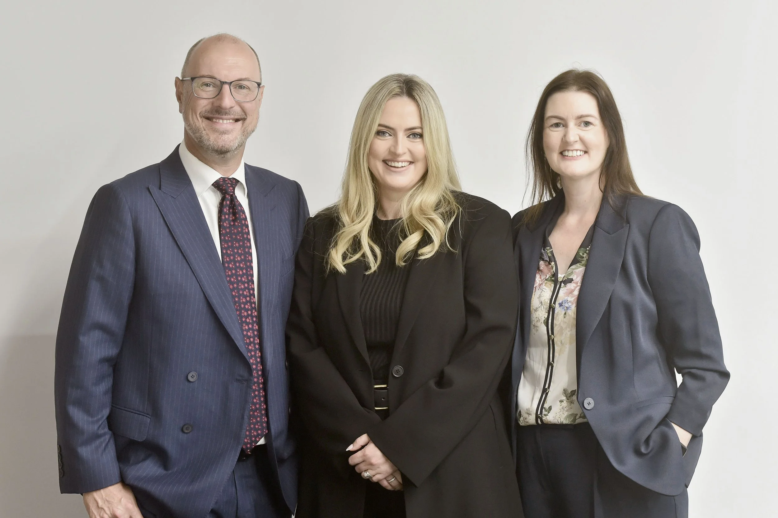 Three employment lawyers dressed people standing together against a plain white background, smiling at the camera.