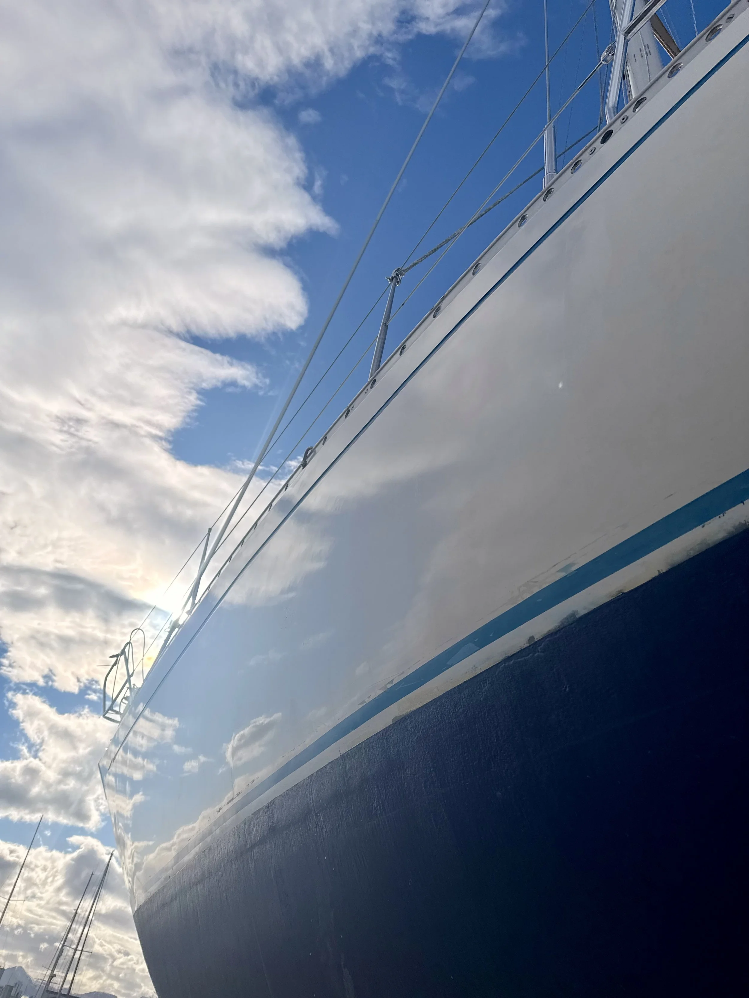 Close-up of Lady B, an IW40 sailboat from below, showing the hull, rigging, and blue sky with clouds.