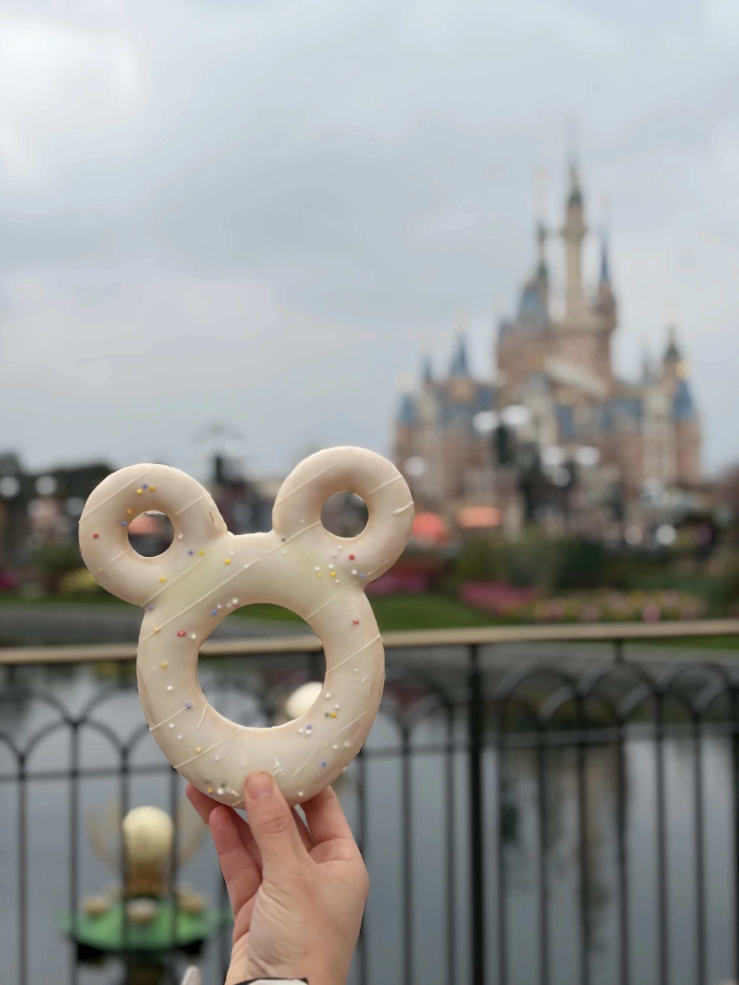 Erin Davis, LCSW & ADHD Therapist holding a white chocolate Mickey Mouse-shaped pretzel with colorful sprinkles in front of a castle at Disneyland.