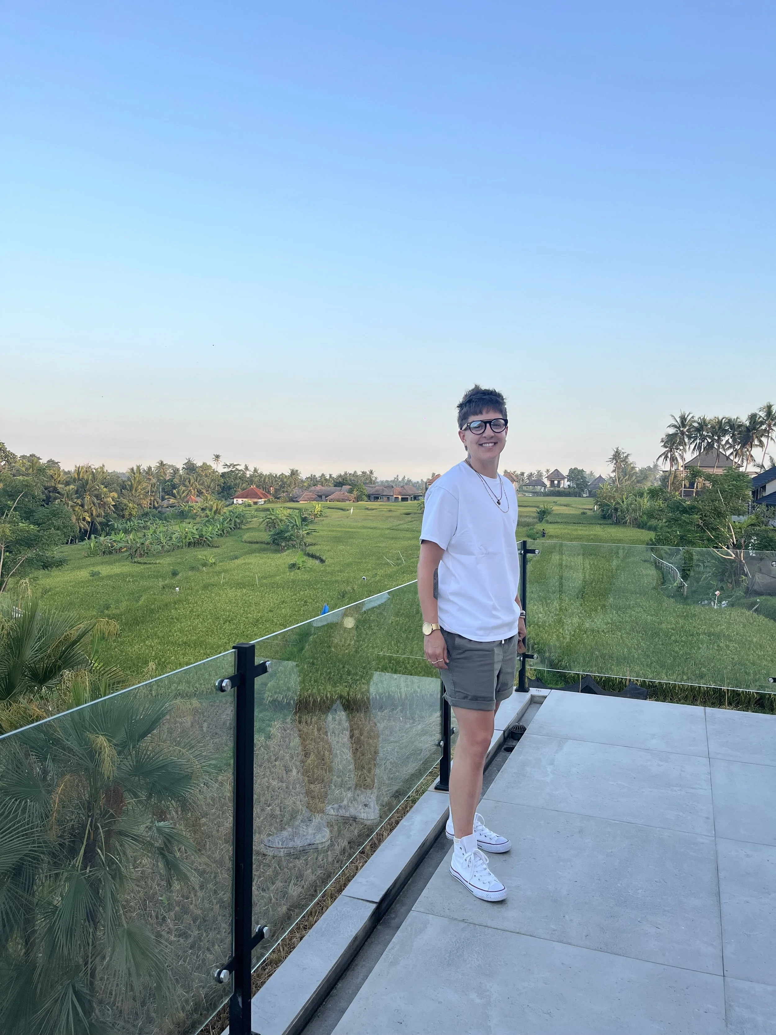 Erin Davis, LCSW & ADHD Therapist standing outside on a patio overlooking a lush green landscape with palm trees and houses under a clear blue sky.