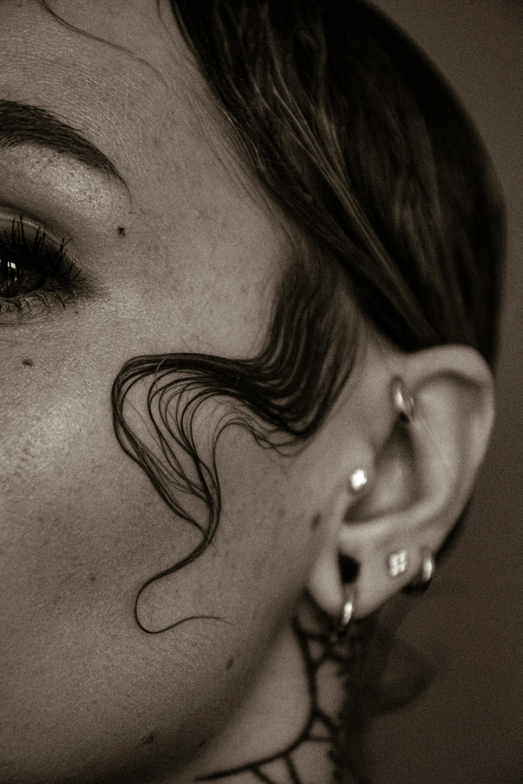 Close-up of a person's face with focus on an eye, eyebrow, and facial skin. The person has dark hair, a small nose piercing, and several nose piercings with jewelry.
