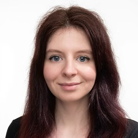 Portrait of a young woman with fair skin, shoulder-length dark hair, and blue eyes, smiling slightly, against a plain white background.