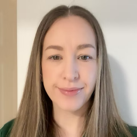 A young woman with long straight hair smiling at the camera, indoors with a neutral background.