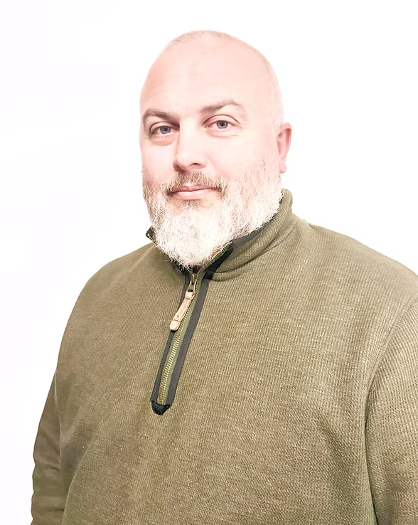 Portrait of a bald man with a beard wearing an olive green quarter-zip pullover, standing against a plain white background.