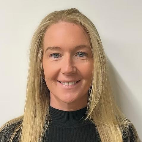 Headshot of a woman with long blonde hair wearing a black top, smiling in front of a plain white background.
