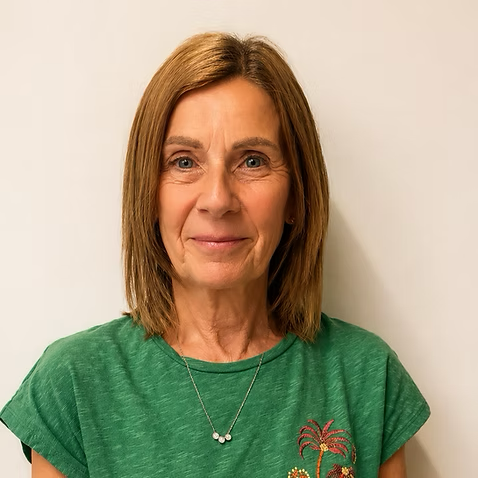 A woman with shoulder-length brown hair wearing a green t-shirt and a necklace, standing against a white background.