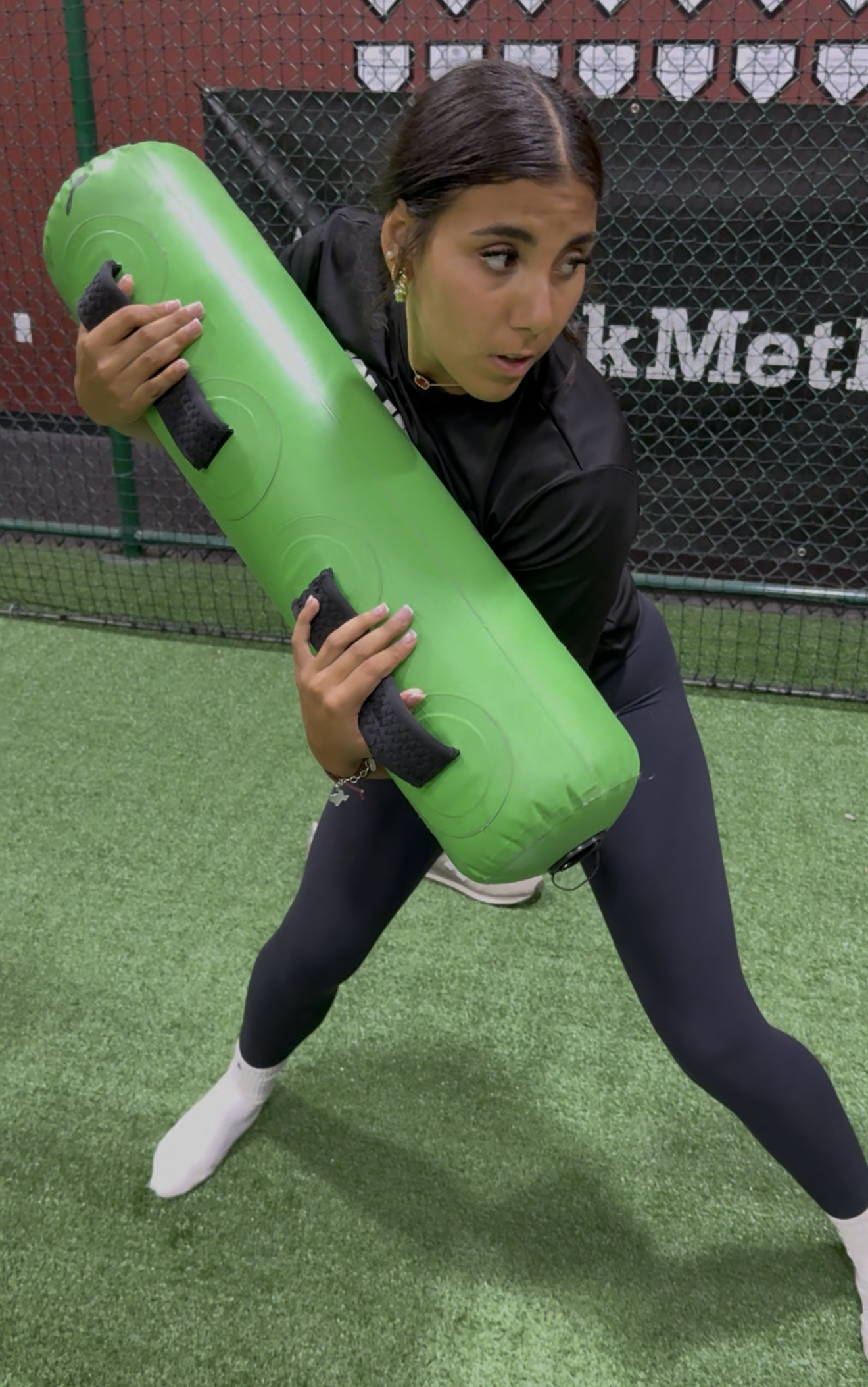 Woman in athletic attire holding a green roller on a green turf training field.