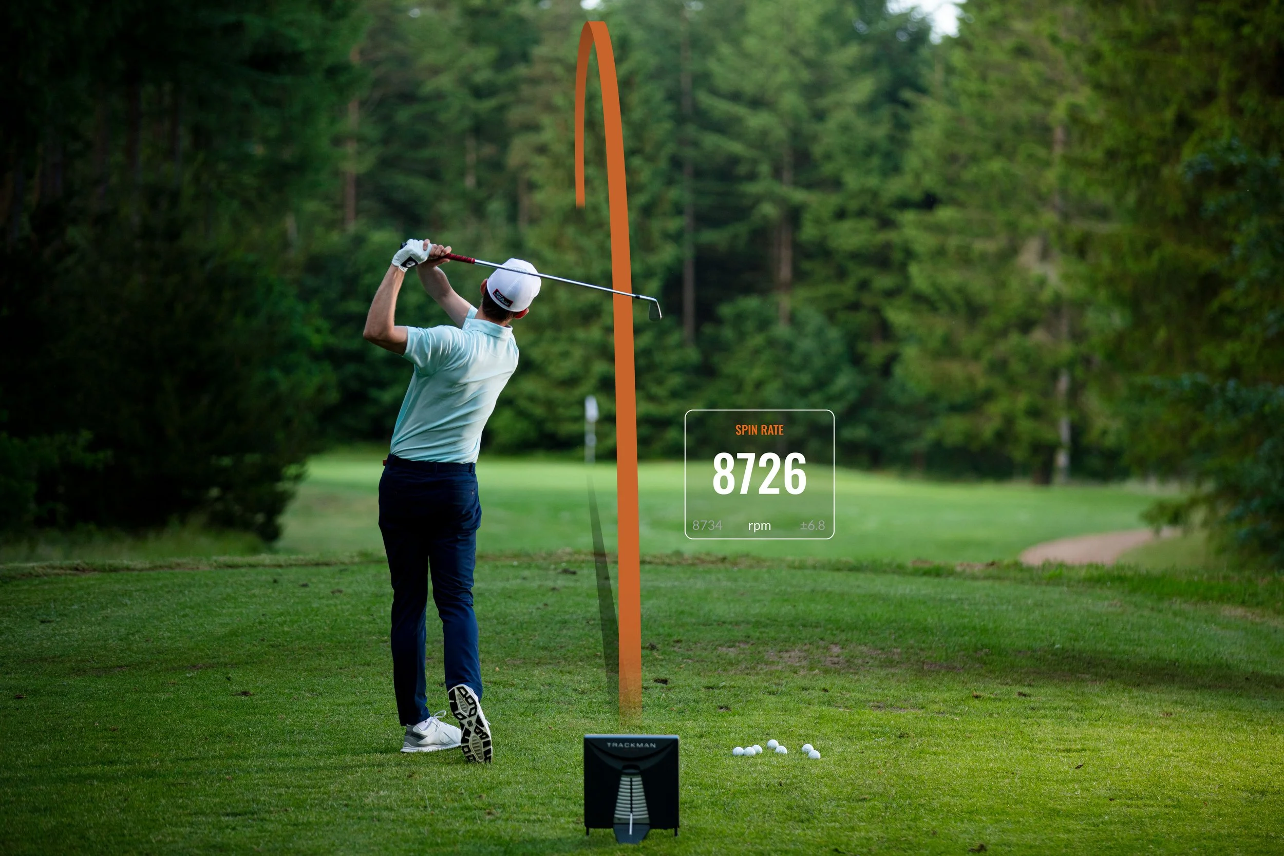 A golfer takes a swing on a golf course with a screen showing a spin rate of 8726 rpm and a background of trees.