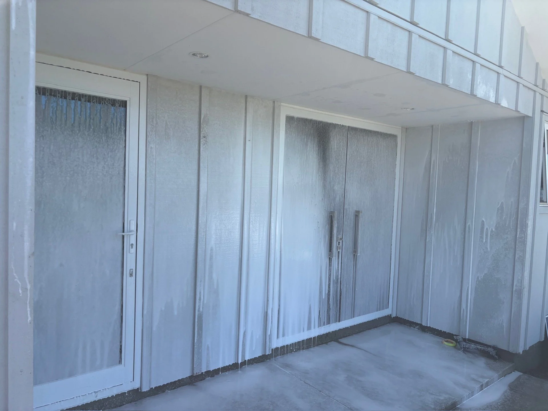 Building wash site with soft wash applied to the wall and doors, showing ongoing building wash.