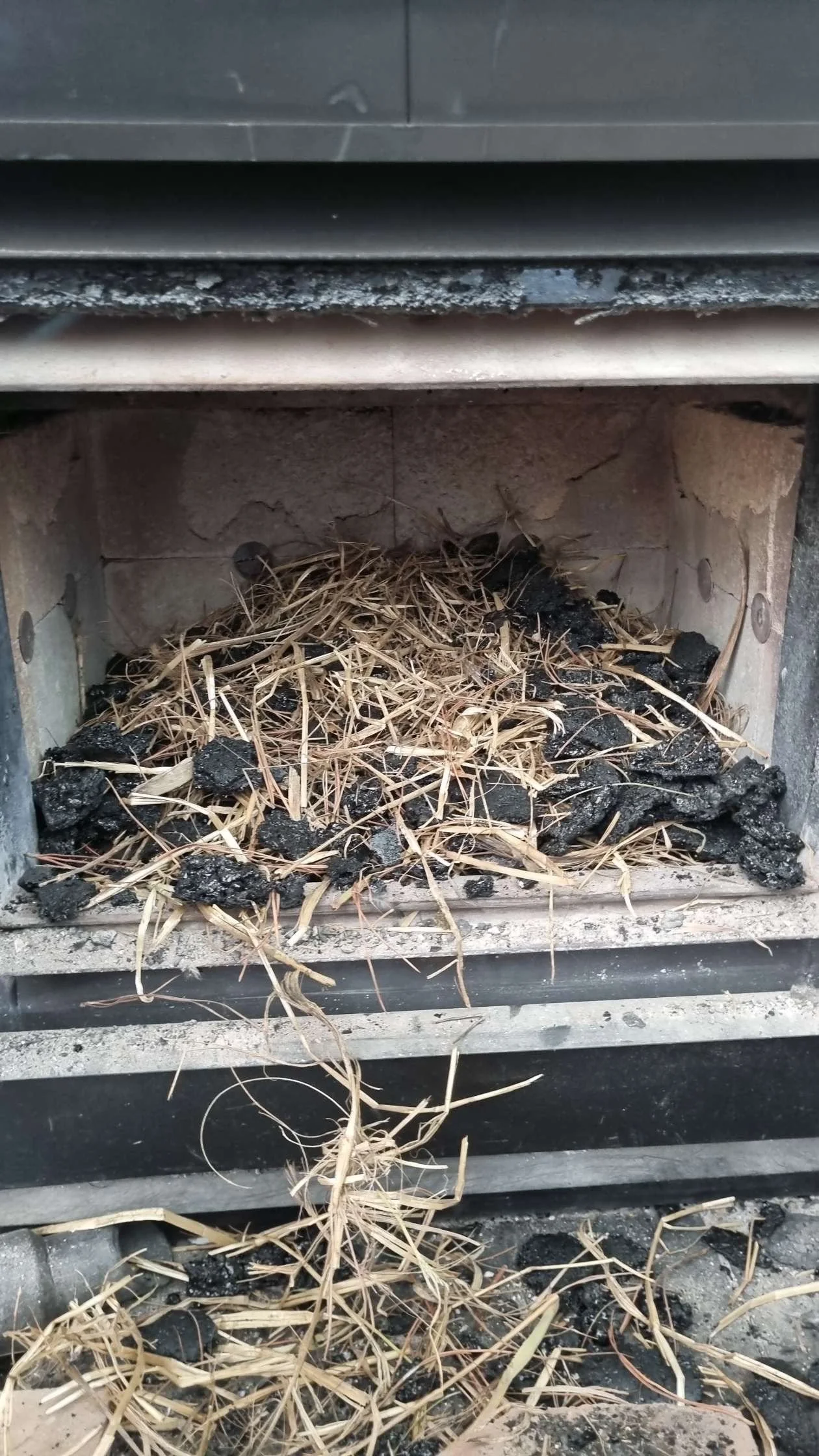 A close-up of a chimney with a buildup of black soot, ashes, and dried grass or straw inside.