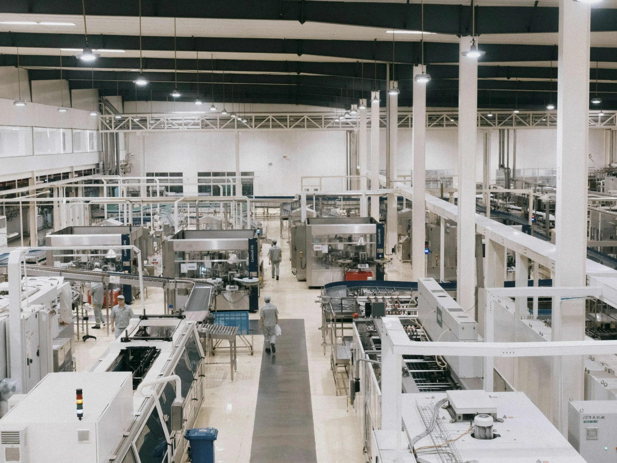 Cleanroom or laboratory with industry equipment, technicians working, white and gray color scheme, high ceilings, and bright lighting.