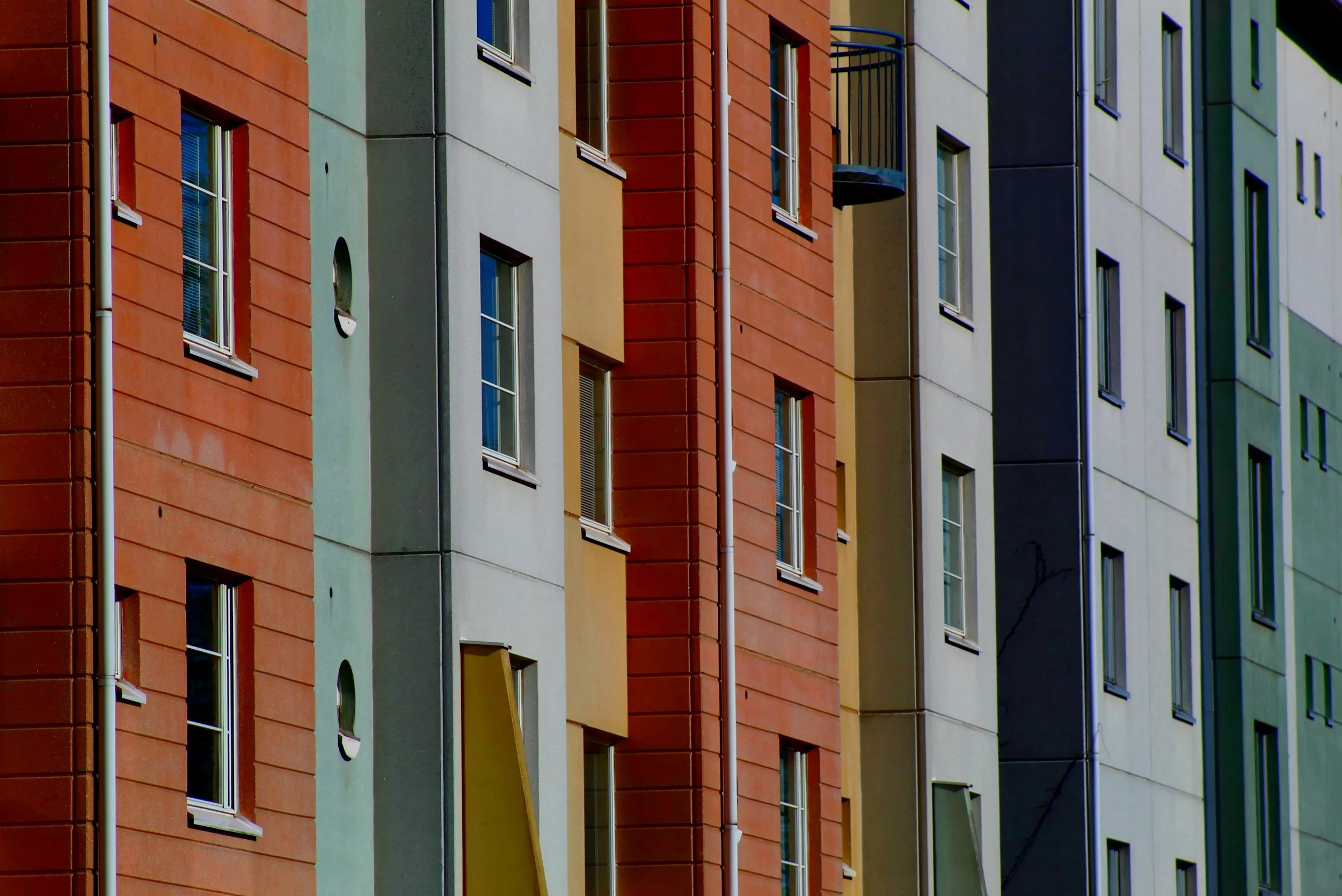 Colorful apartment building with various colored sections and several windows, some with open curtains, and a small balcony.