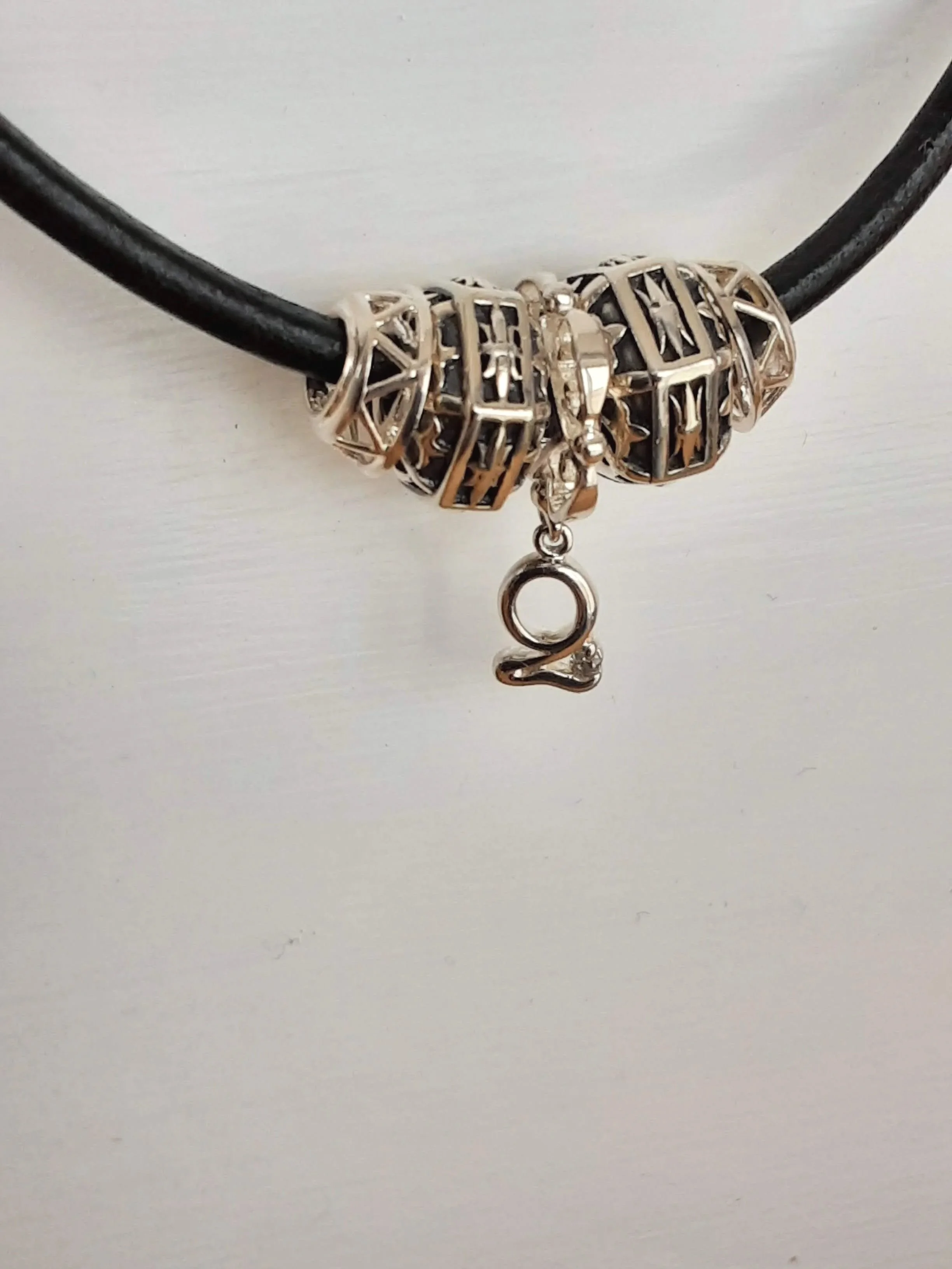 Close-up of a black string necklace with multiple silver decorative beads and a small silver charm in the shape of a woman.