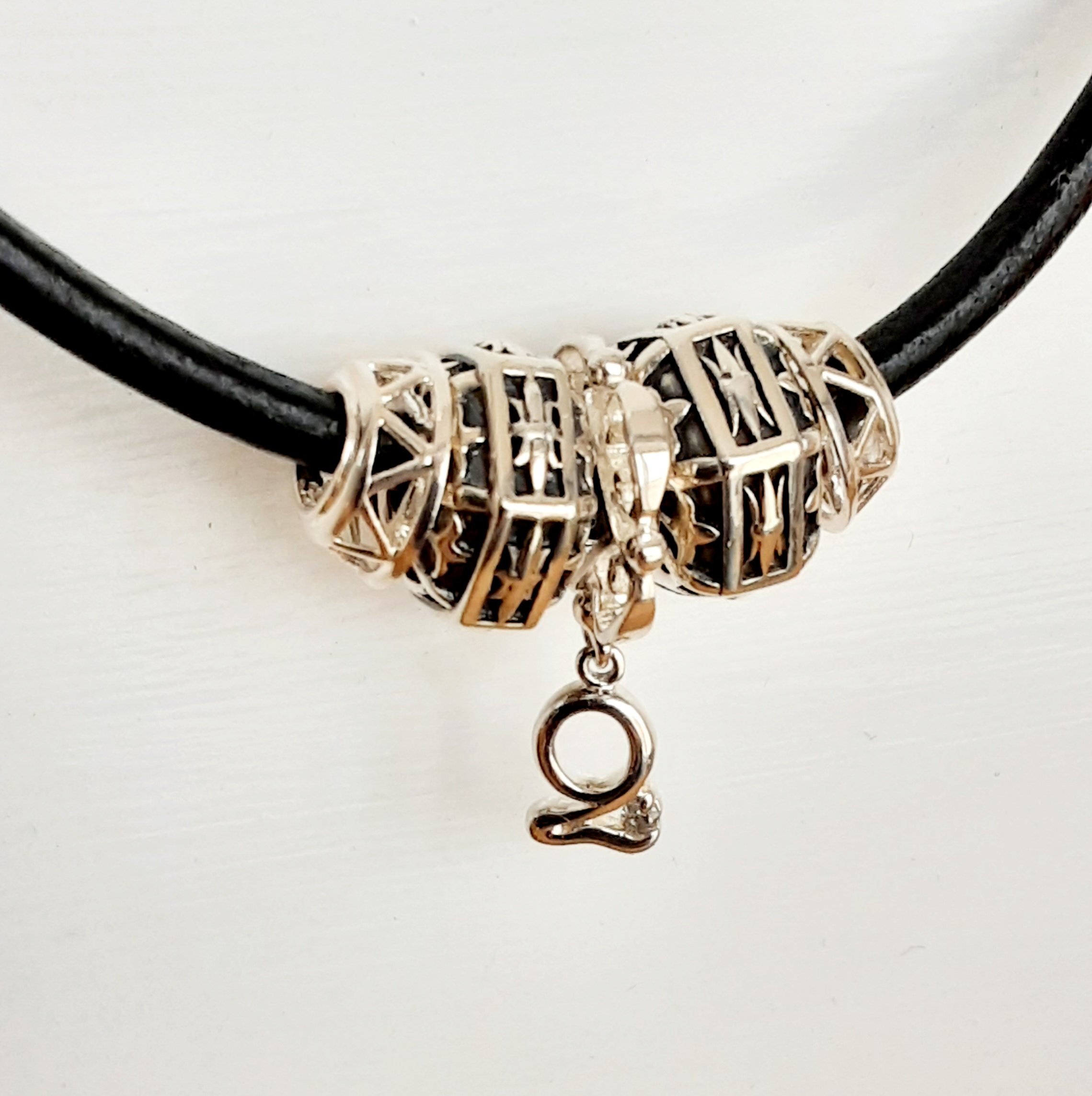 A close-up of a jewelry pendant in the shape of the letter 'Y', made of a metallic material with an openwork geometric design, hanging from a black cord.