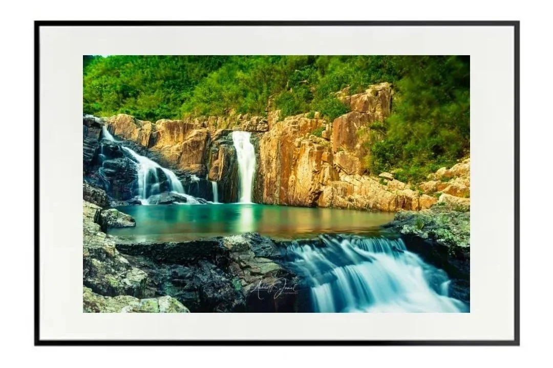 Framed fine art print mockup of a long-exposure waterfall landscape in Sai Kung, Hong Kong, presented in a thin black frame on a white wall.