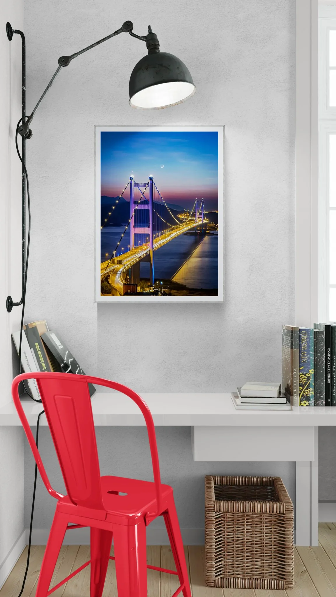 Framed photograph of an illuminated suspension bridge at night hanging on a gallery wall above a red chair.