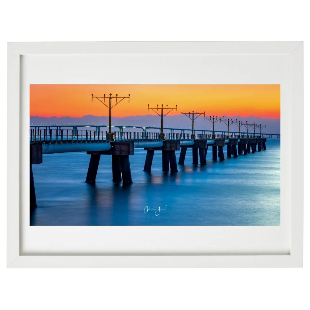 Minimalist white framed landscape photography print of the Hong Kong Aircraft Maintenance Area at dusk. This bright framed wall art showcases a vibrant orange and blue seaside sunset.