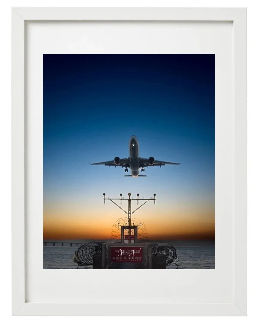 A framed aviation fine art print of a commercial airplane landing at sunset, featuring a wide white mat board and a minimalist white frame.