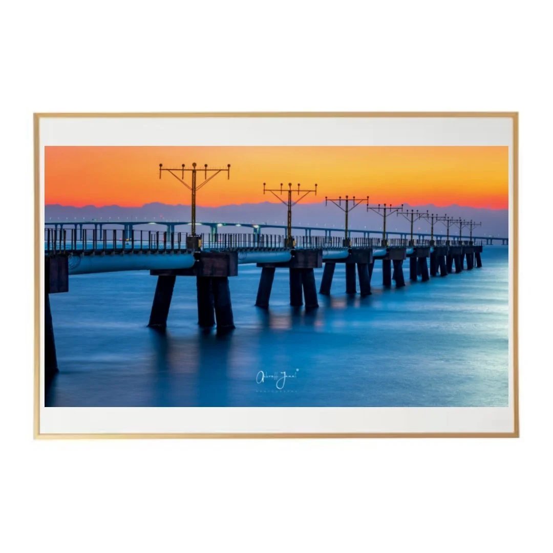Blue Hour Radiance AJ8399 fine art photo by Ashraff Jamal, presented in an elegant gold frame with a wide white mat border, showcasing the Hong Kong Airport landing lights pier at sunset.