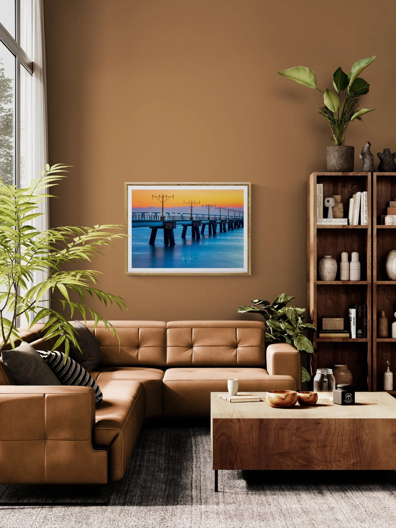 Modern living room interior mockup featuring a warm terracotta brown wall with a large framed ocean sunset art print hanging above a tan leather sectional sofa.