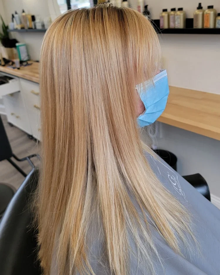Woman with long blonde hair wearing a face mask, sitting in a salon chair.