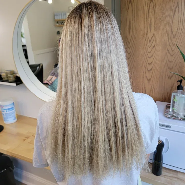 Back view of a woman with long, straight blonde hair in a salon or hair studio.