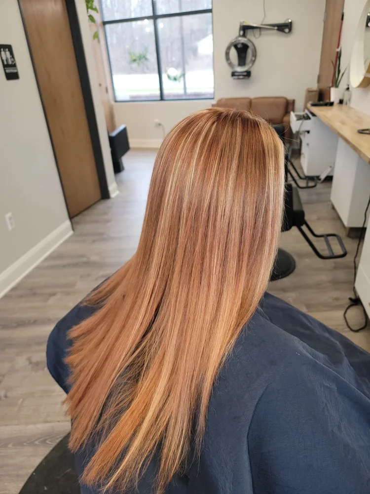 A woman with straight, shoulder-length, copper-colored hair sitting in a hair salon.