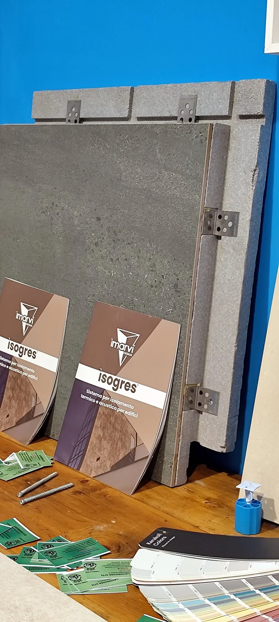 Una mostra di campioni di materiali da costruzione, come pannelli di isolamento e rivestimenti, con volantini pubblicitari e strumenti di misurazione sopra un tavolo di legno.