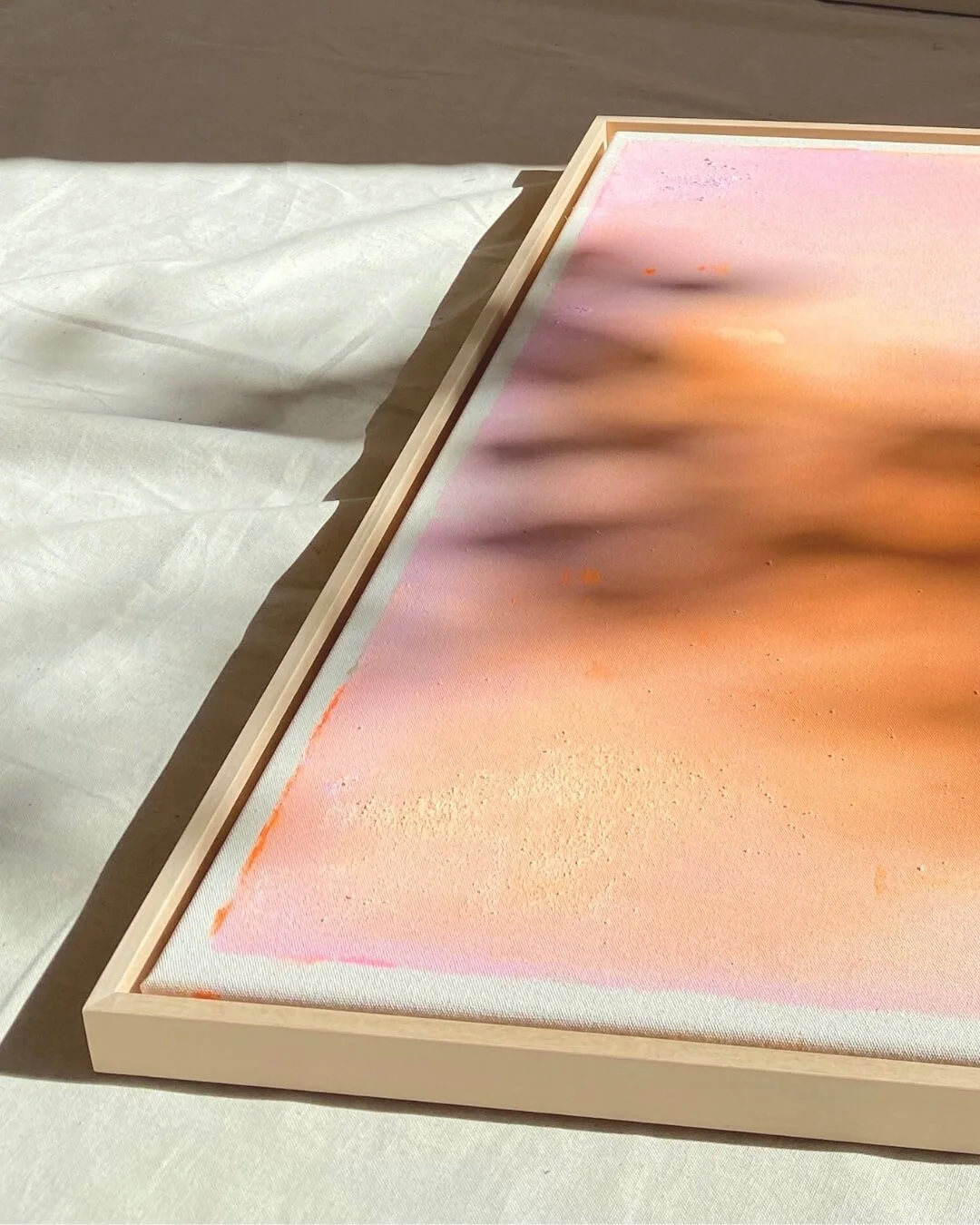 Angled shot of the framed original painting Peachy Glow Dust I, highlighting how light catches the textured surface and soft peach tones by Vanessa Ochi