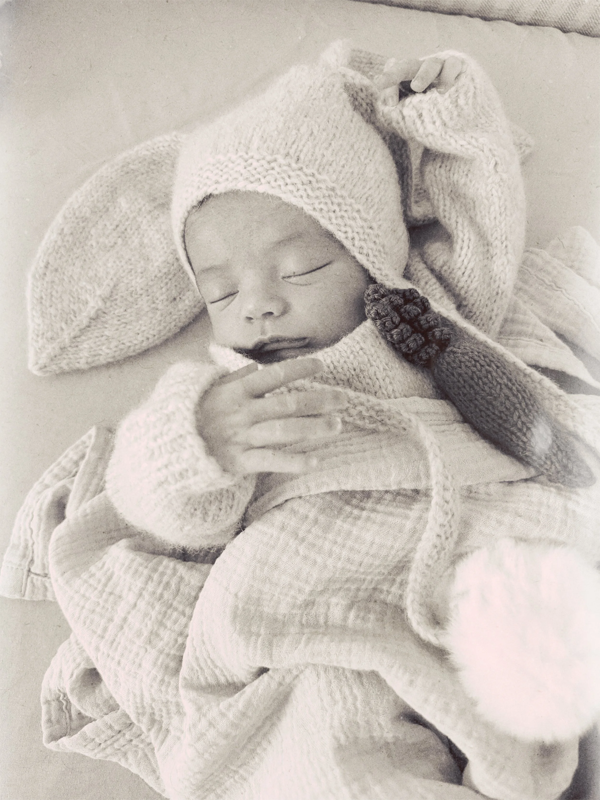 A sleeping baby wrapped in a knitted blanket and wearing a knitted hat.