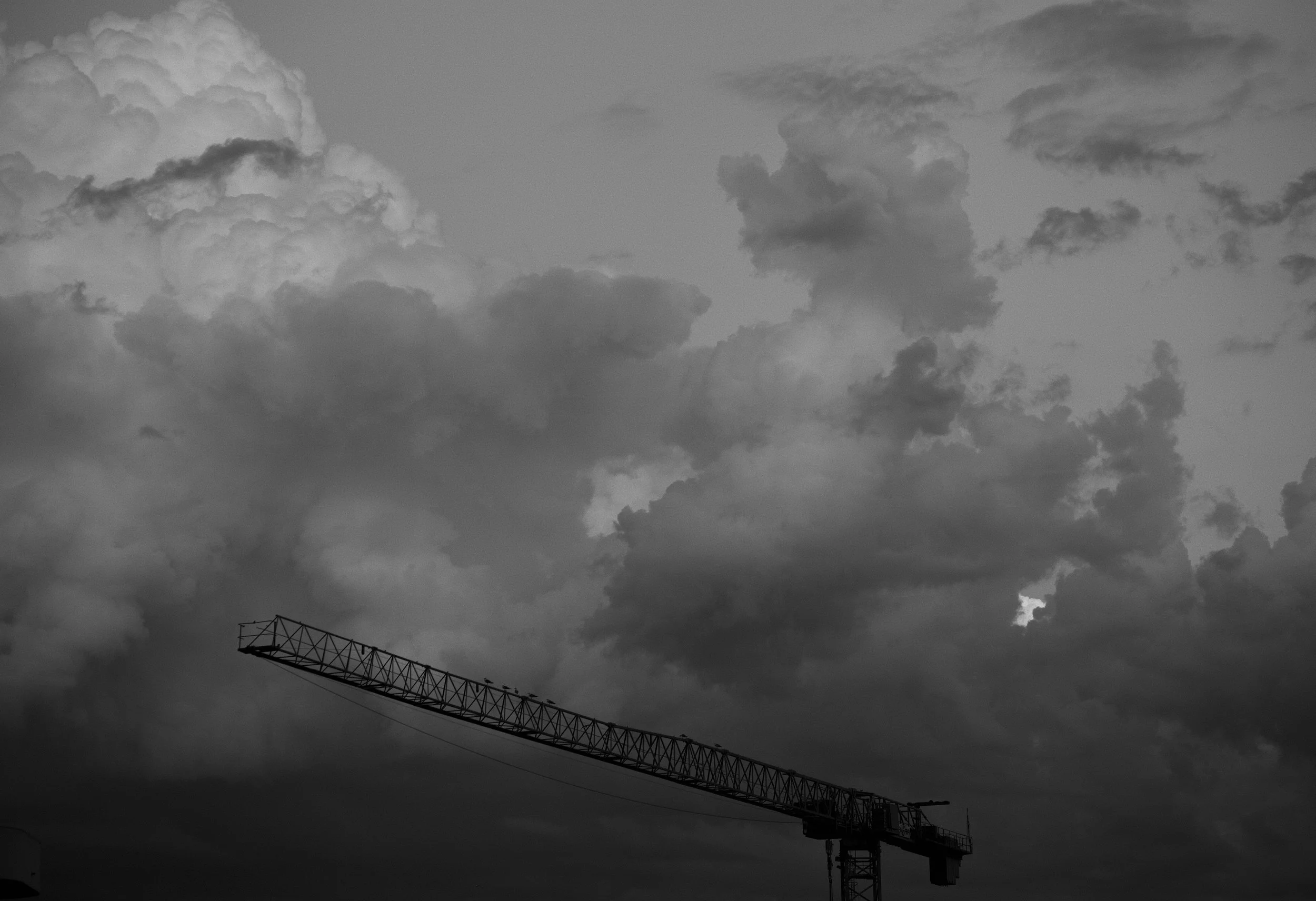Black and white photo of a construction crane against a cloudy sky.