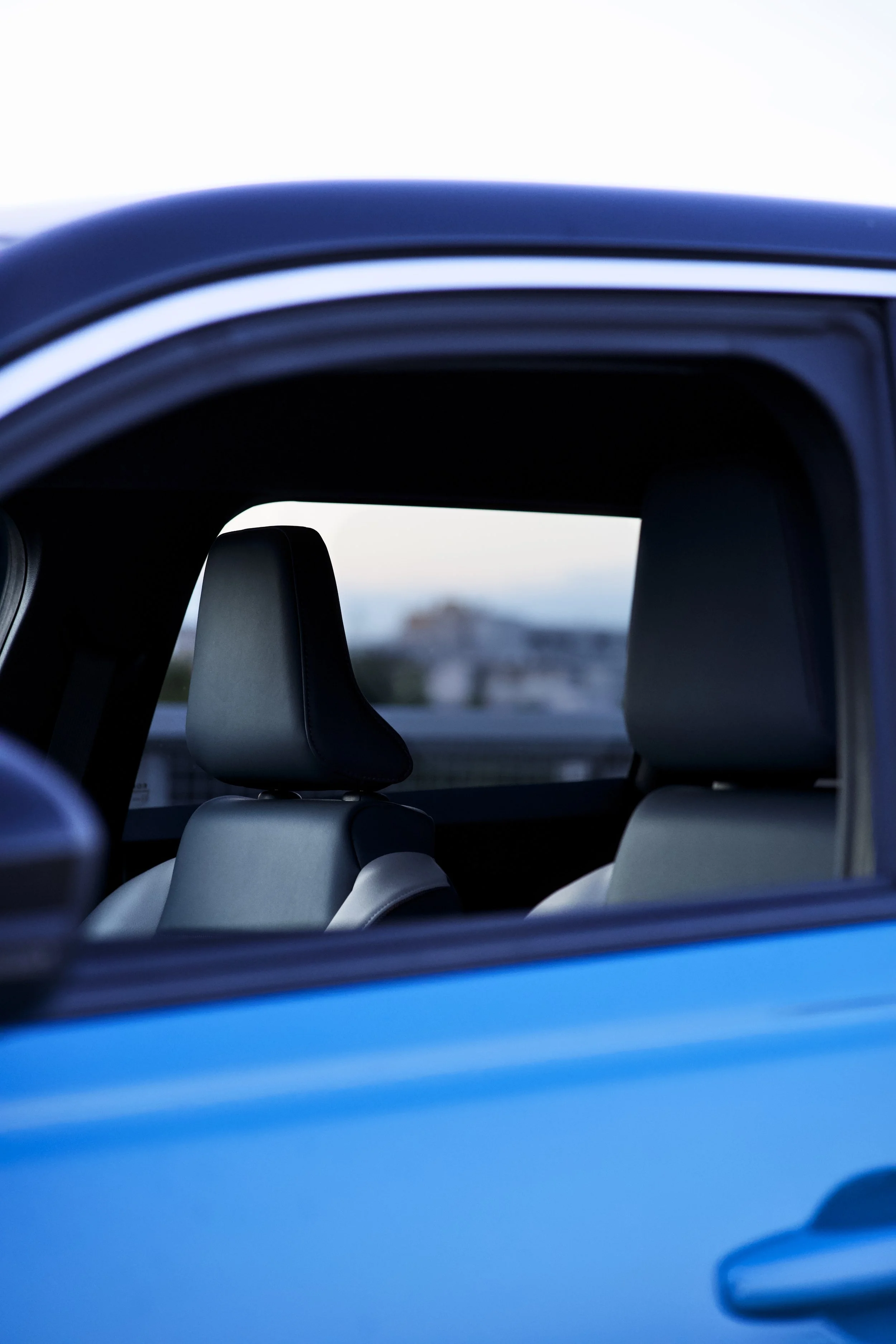 The image shows the interior of a car, viewed through the rear window. Two headrests are visible, with a blurred outdoor background and part of the car's window frame framing the scene.