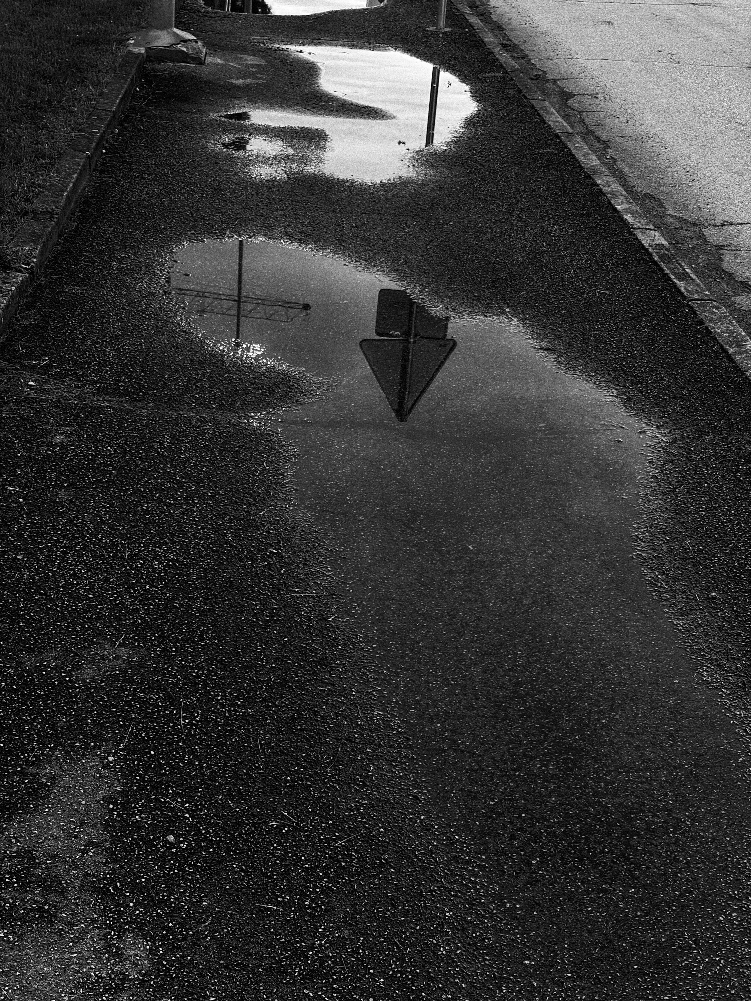 A street sidewalk with a puddle of water reflecting a stop sign and a utility pole.