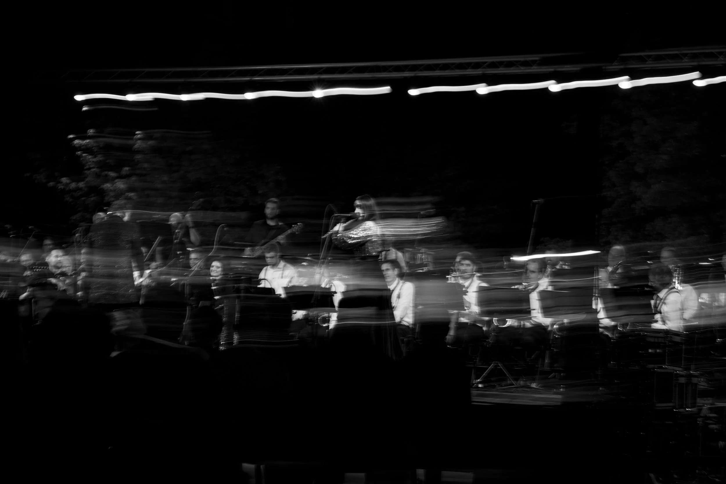 Black and white photo of a band performing on stage at night, with some motion blur.
