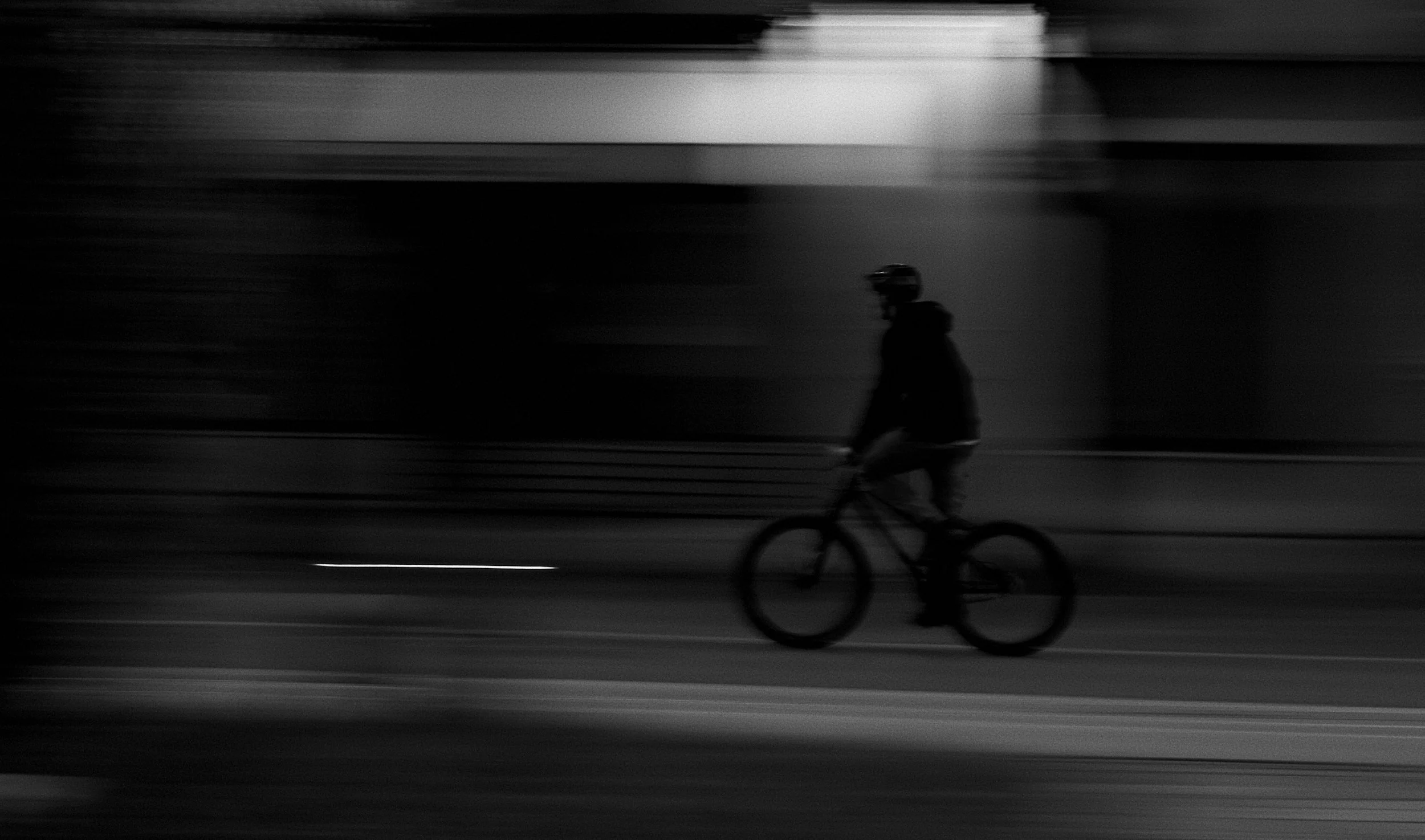 A person riding a bicycle along a dark street at night, with motion blur and illumination from streetlights.