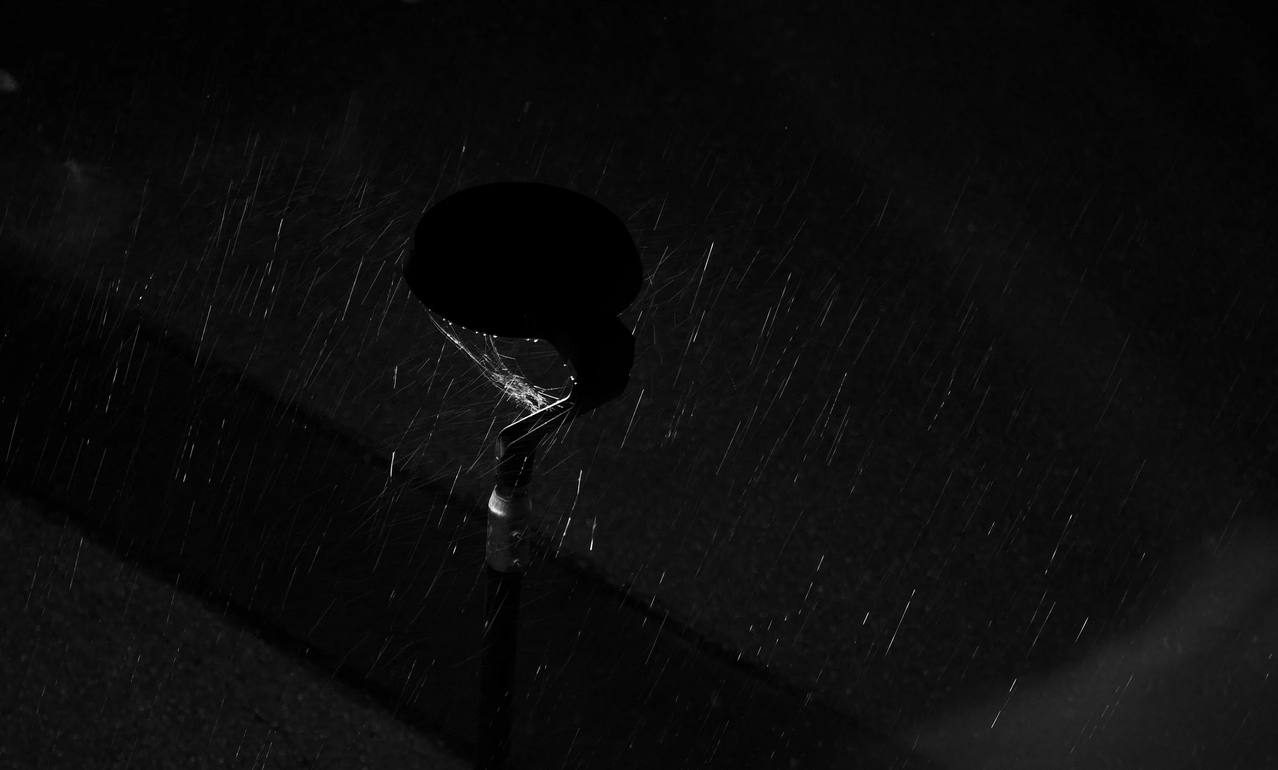 Black and white photograph of a microphone with rain surrounding it, illuminated softly in the darkness.