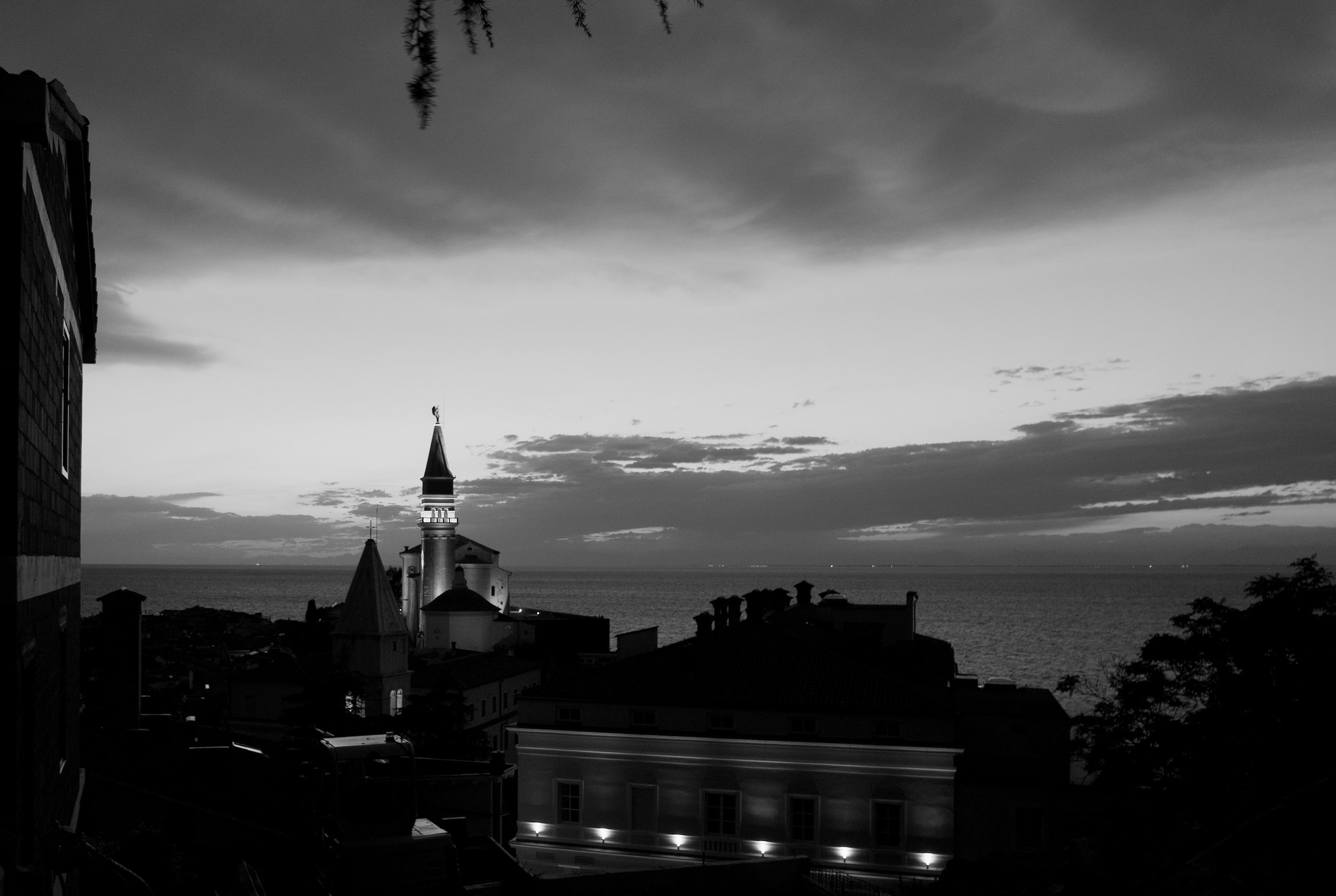Black and white photo of a seaside town with a prominent church steeple, rooftops, and a cloudy sky over the ocean.