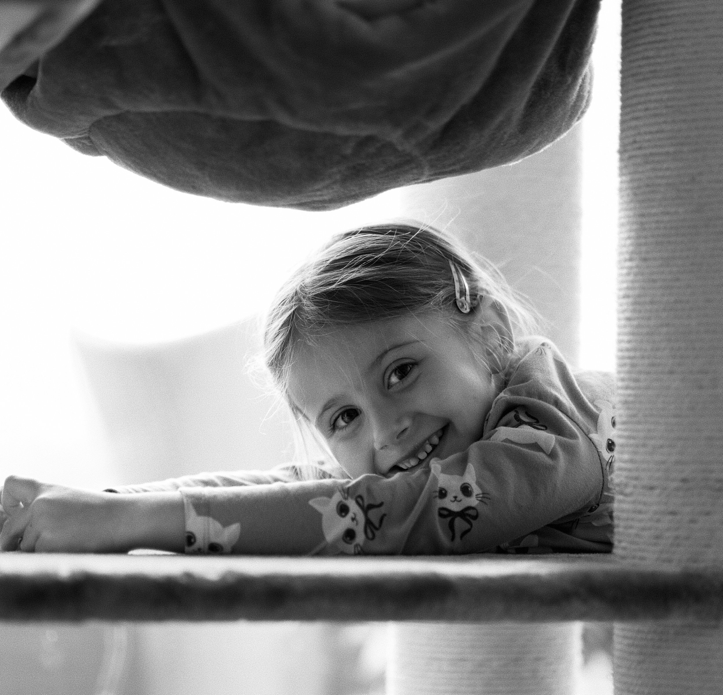 A young girl with glasses smiling close-up shot in black and white, upside down, with a blanket or piece of clothing featuring cat illustrations.