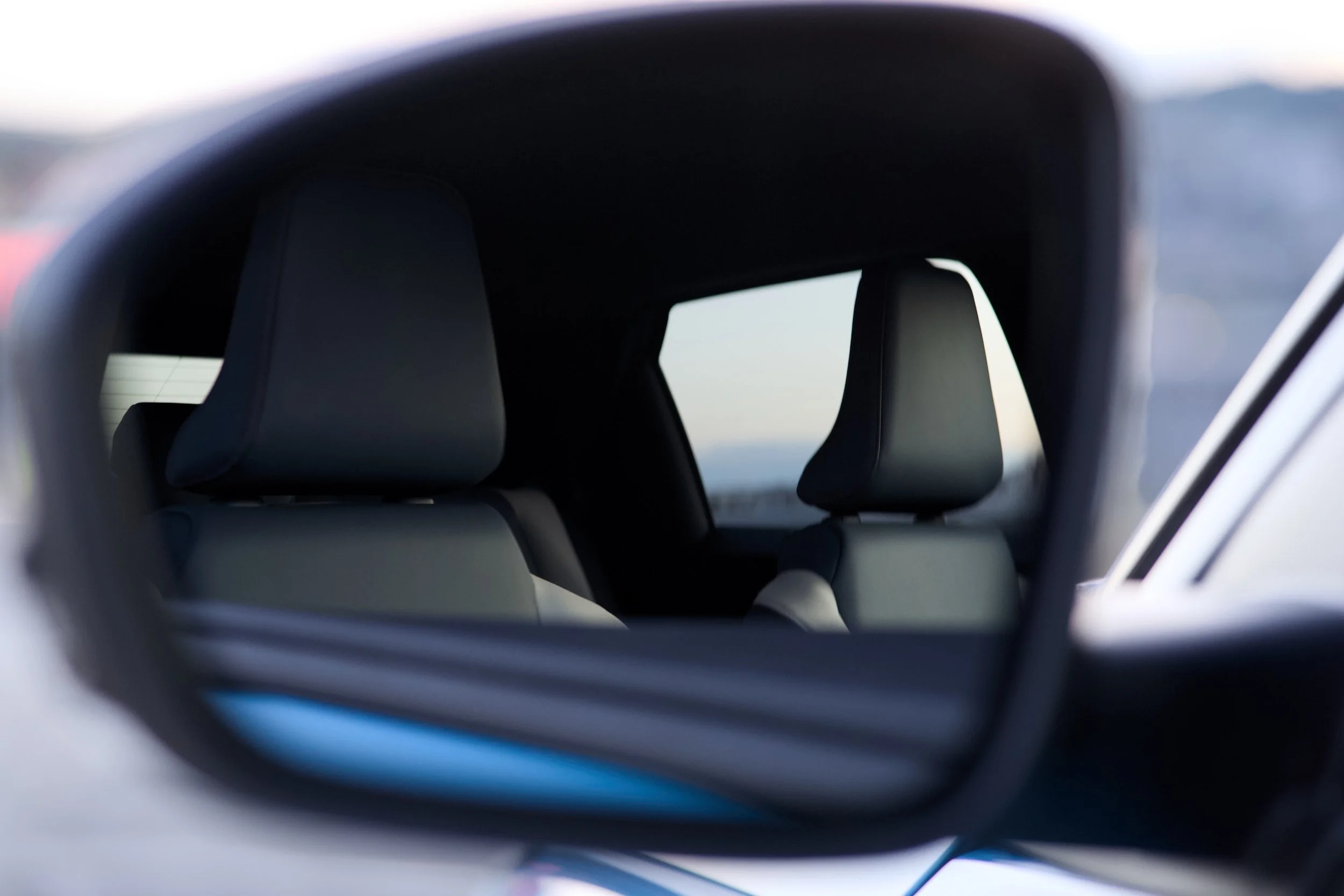 View through a vehicle's side mirror showing the back seats and headrests of the car's interior.