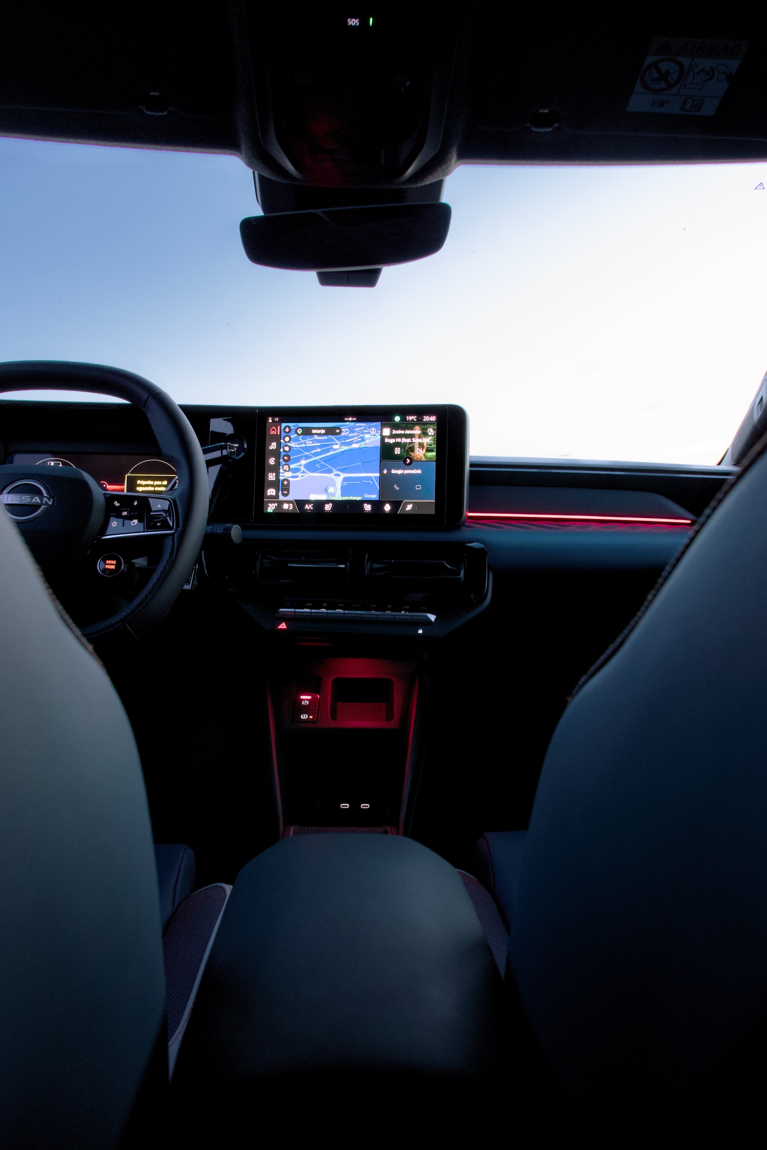 Inside a Nissan vehicle showing the dashboard and the view through the windshield, with the sky visible outside and the car's interior illuminated by ambient lighting.