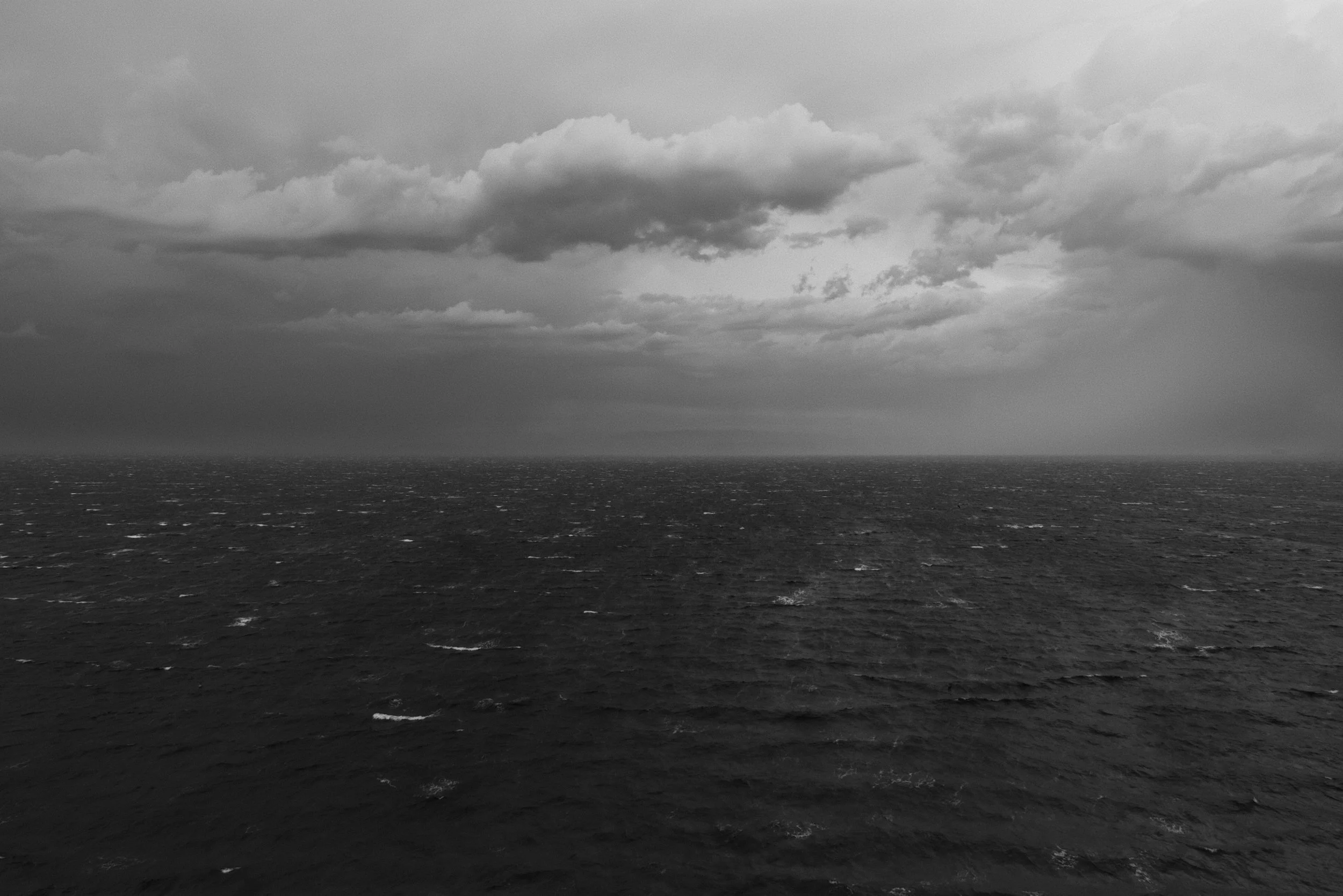 A black and white photo of a calm ocean under a cloudy sky, with the horizon line separating the sea and the sky.