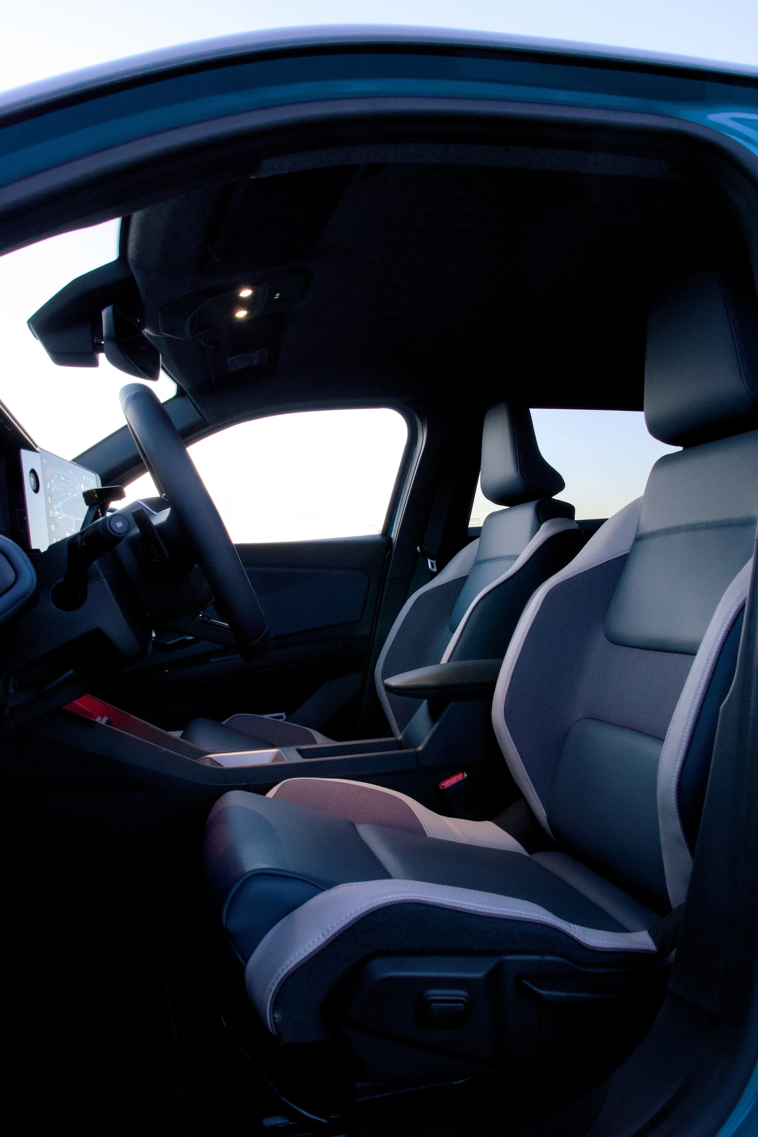 Interior of a modern vehicle with beige leather seats and a digital dashboard, seen from the driver's side with the door open during daytime.