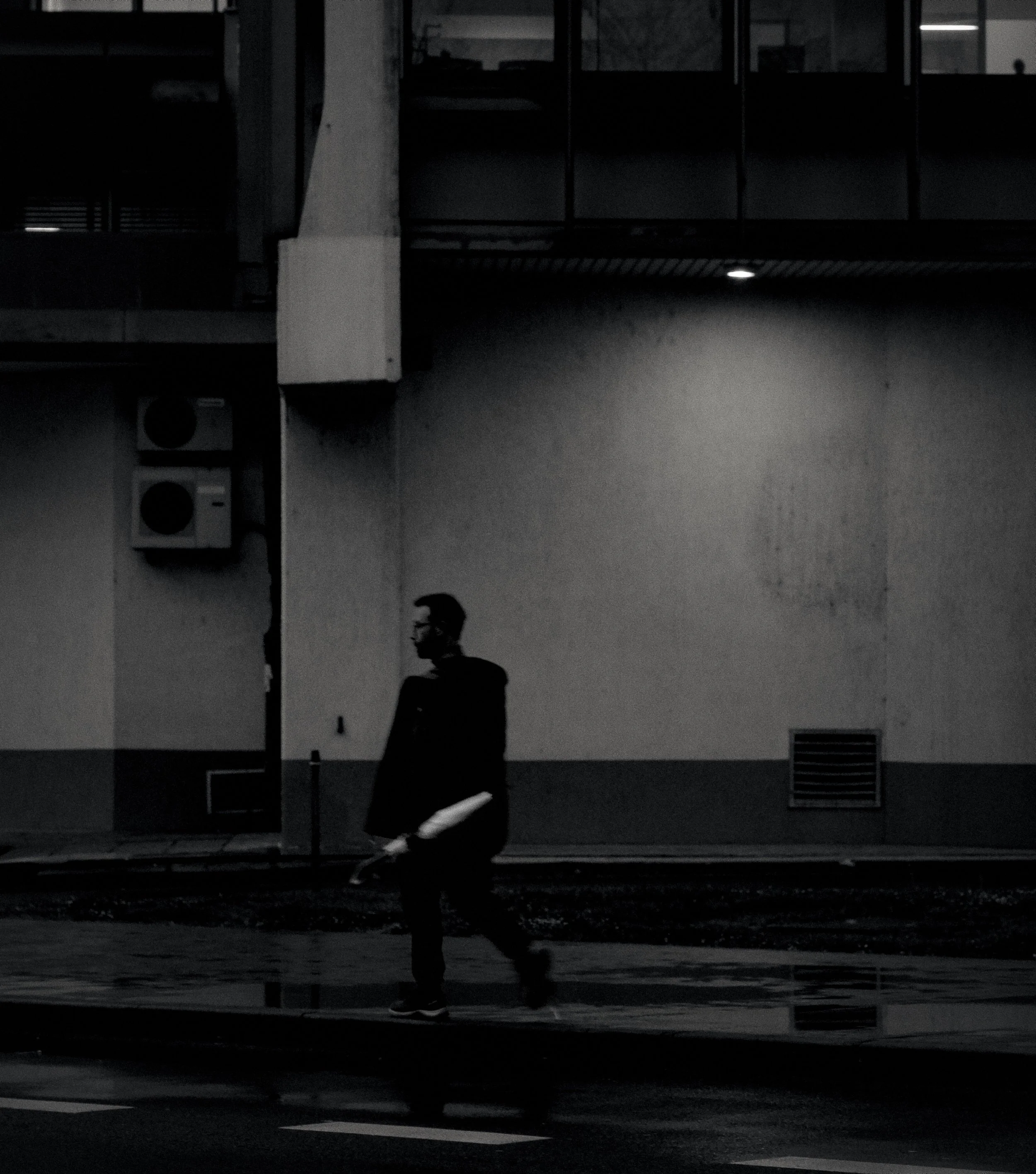 A silhouette of a man walking outdoors at night, reflected in a glass window, with dark background and street elements visible.