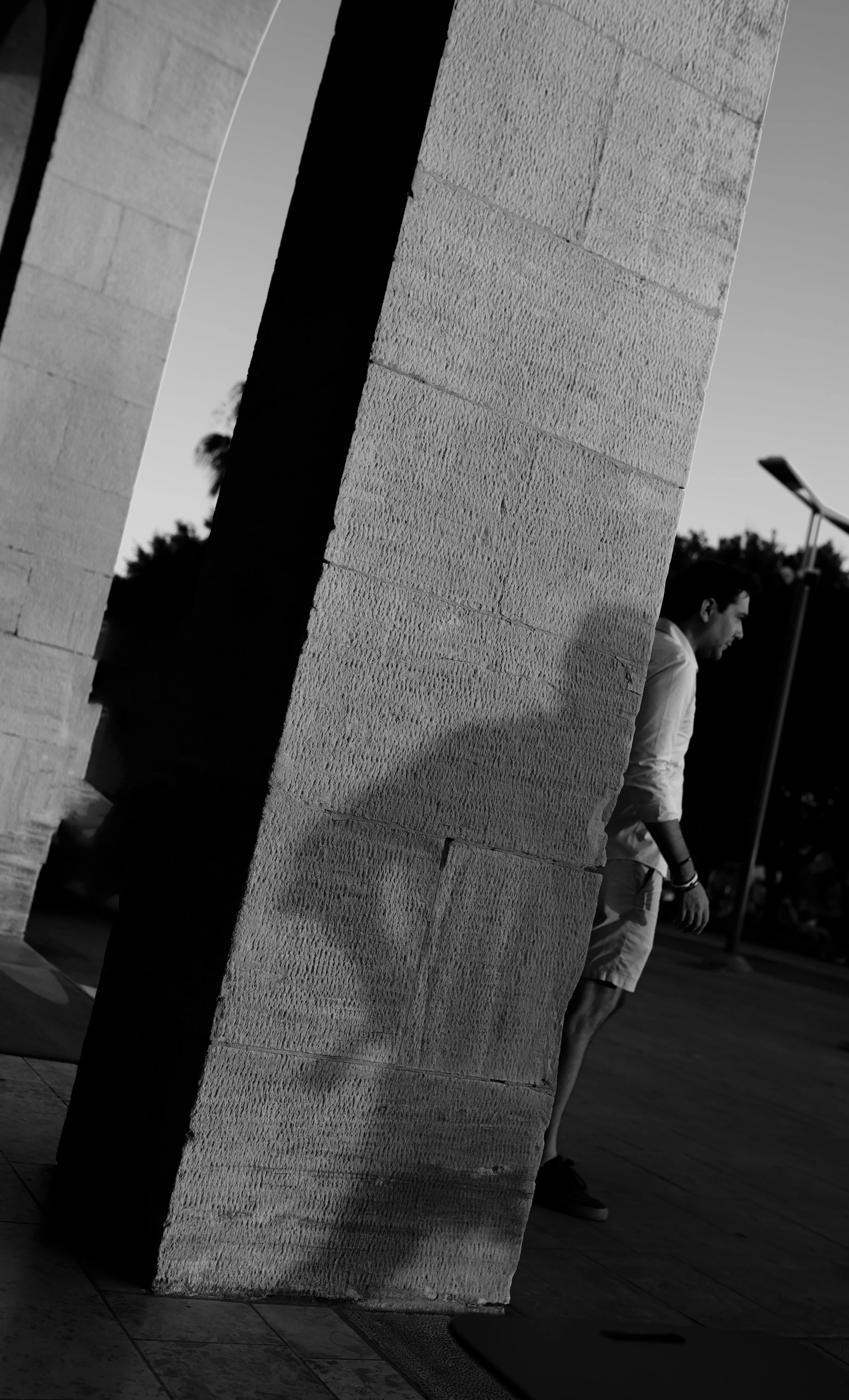 A man walking outdoors near a brick wall in black and white.