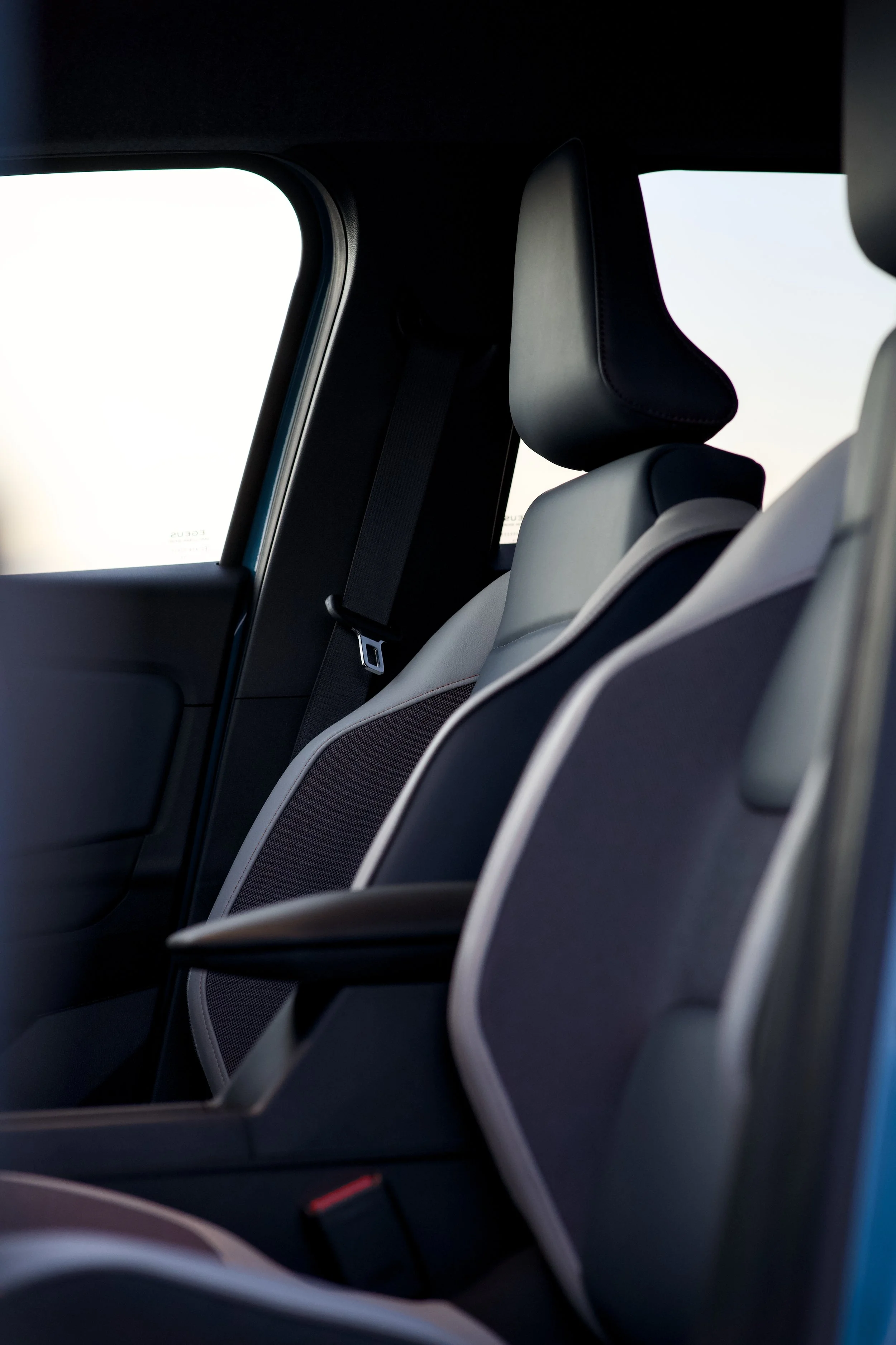 Interior view of a vehicle's back seat area, showing three seats with headrests and a seatbelt, side window, and part of the door frame.