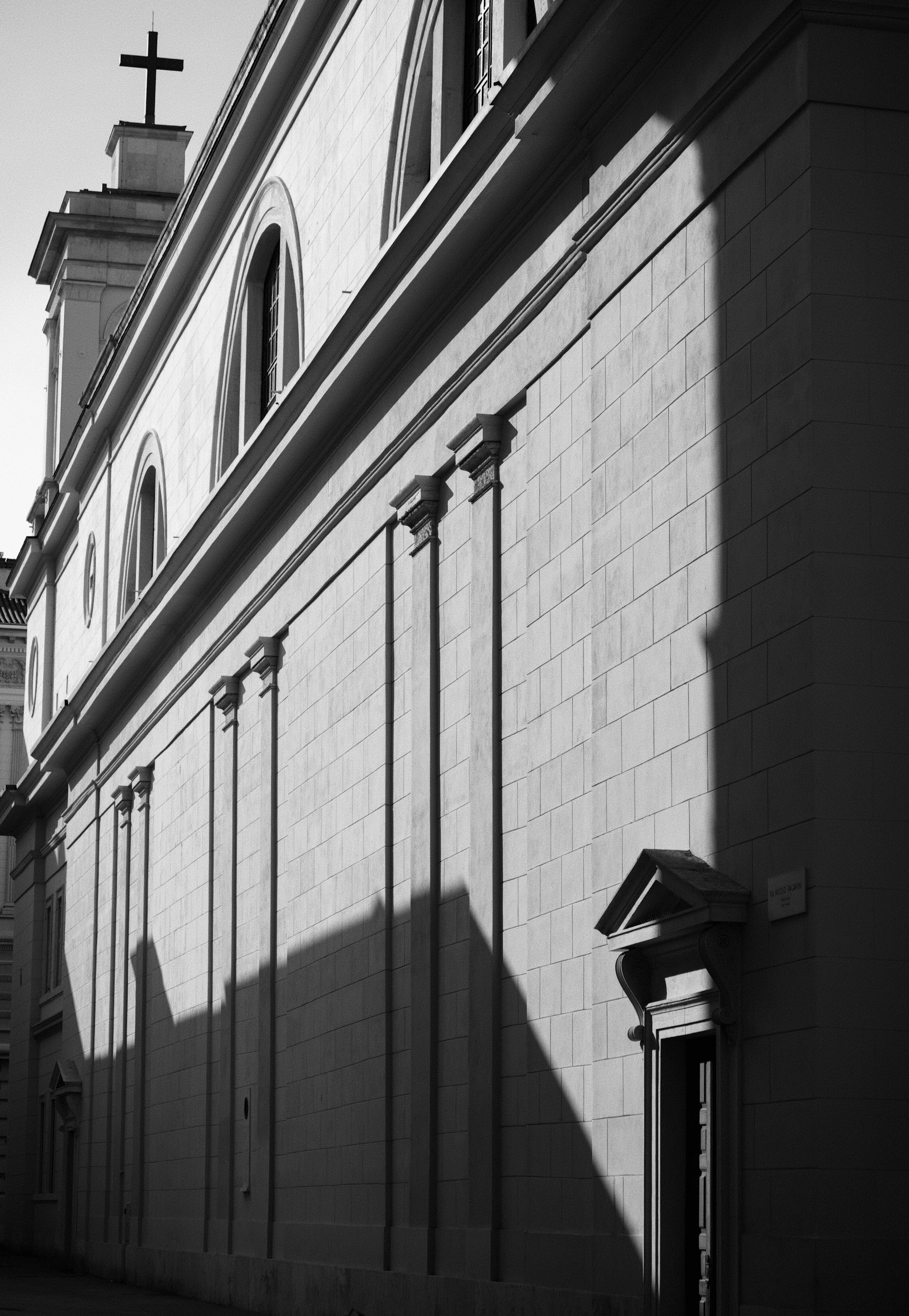 Black and white photo of a church building with a cross on top and arched windows, shadow cast on the facade.