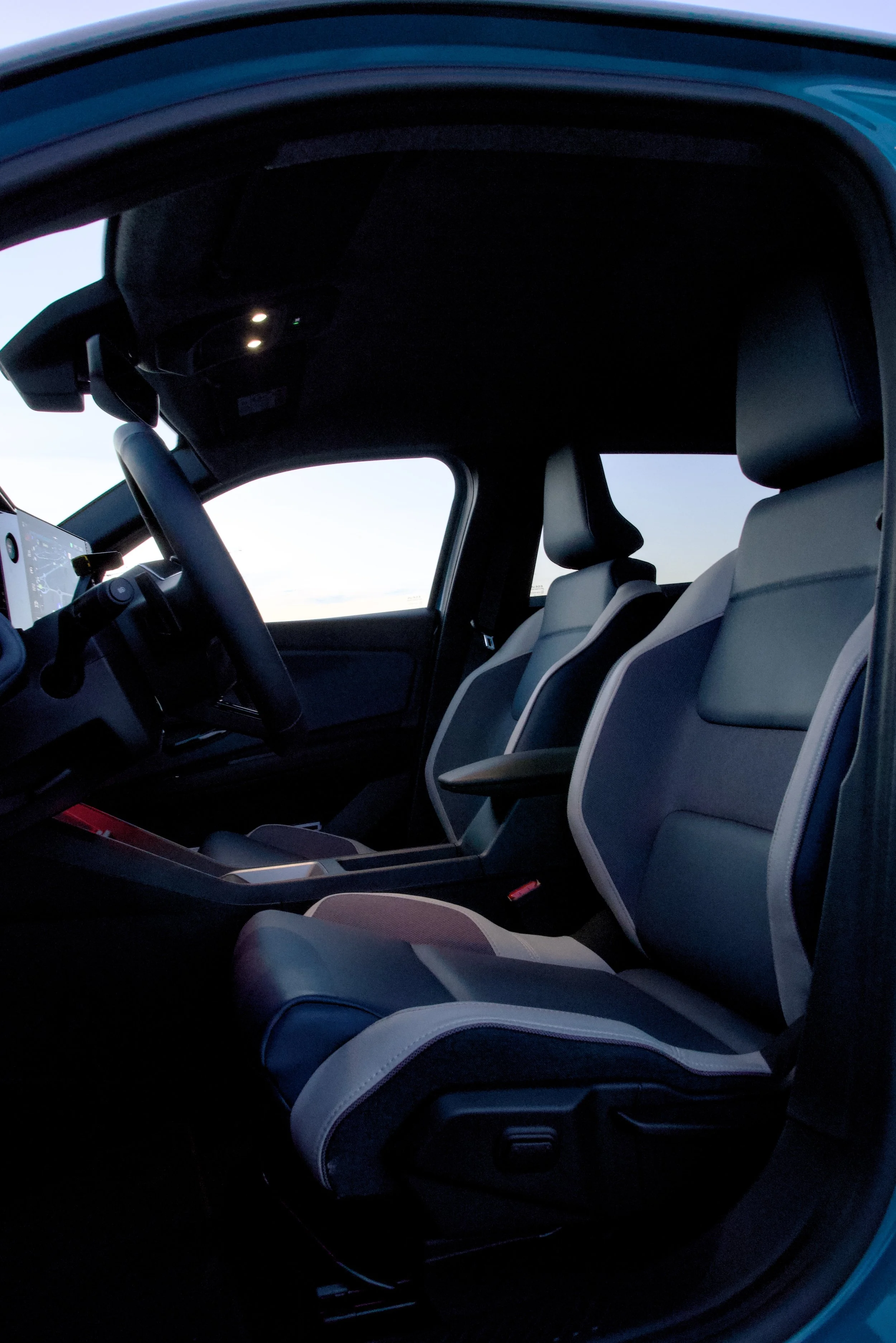 Interior of a modern vehicle with black and light gray seats, a steering wheel, and a digital display visible in the front