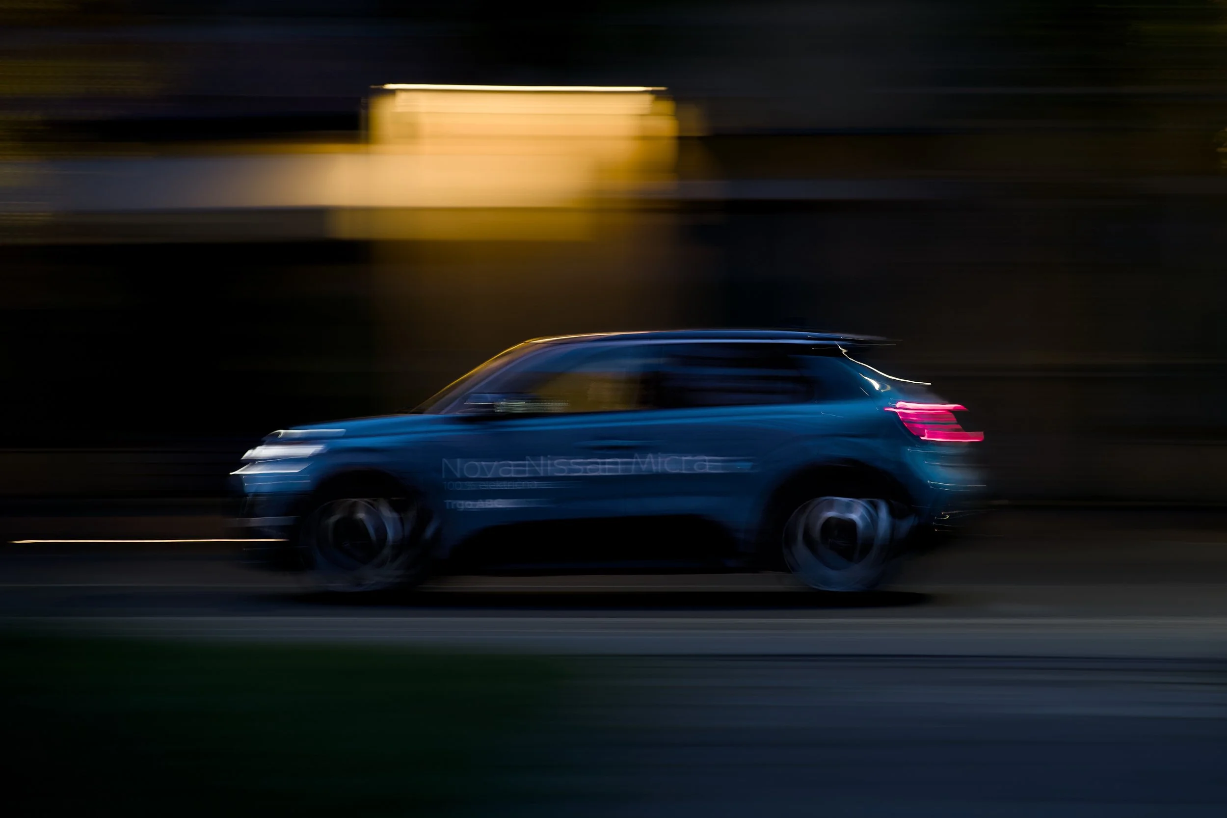 A blue car moving at high speed on a dark road during nighttime, with motion blur and streaks of lights from the vehicle.