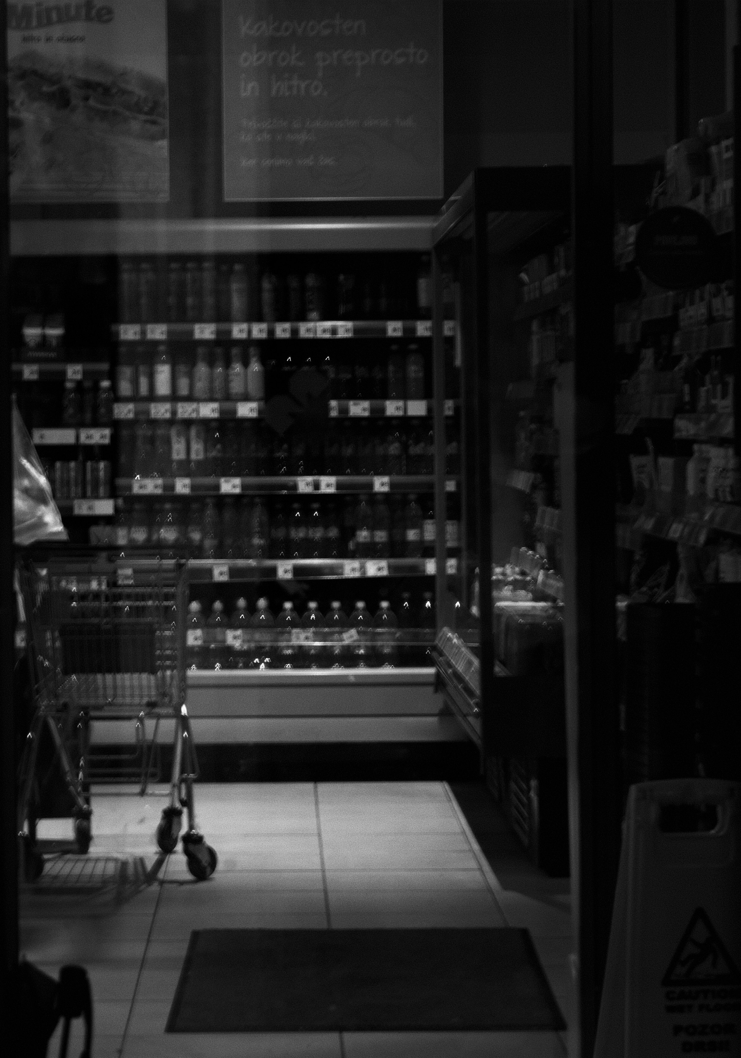 A store aisle with shelves stocked with products, a shopping cart, and a sign in a foreign language.