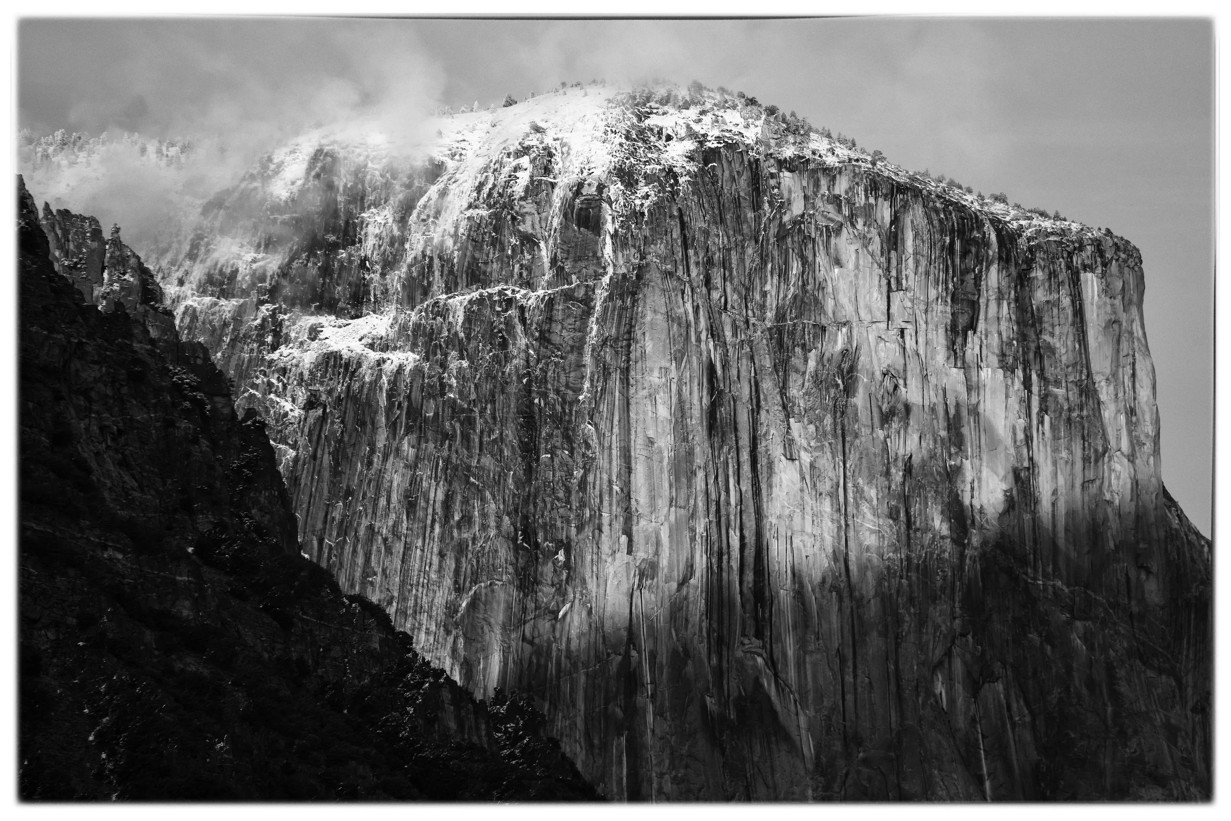 Black and white photo of a snow-covered mountain with cliffs and clouds at Yosemite National Park.